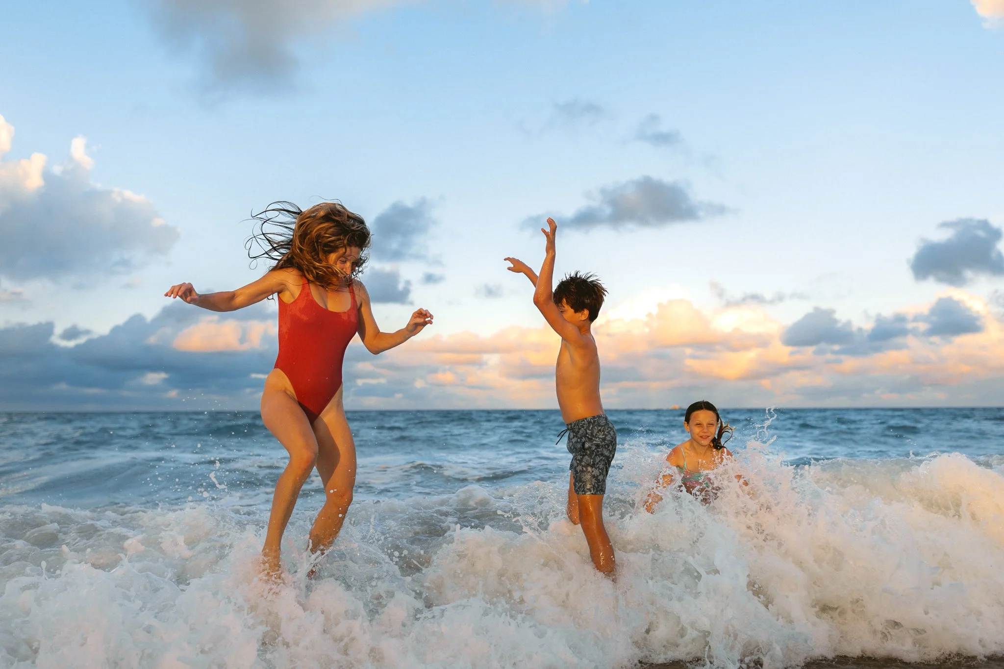 Family playing in the ocean waves during golden hour