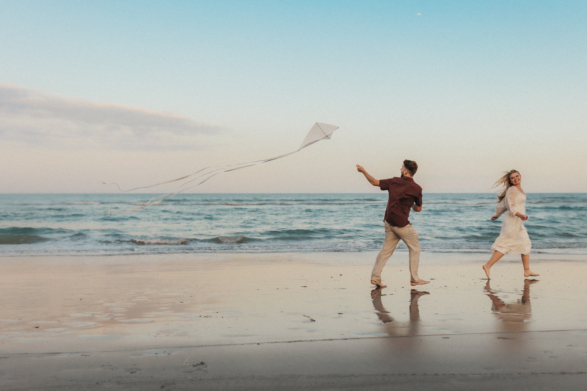 A man and woman flying a kite on the beach with the ocean in the background.