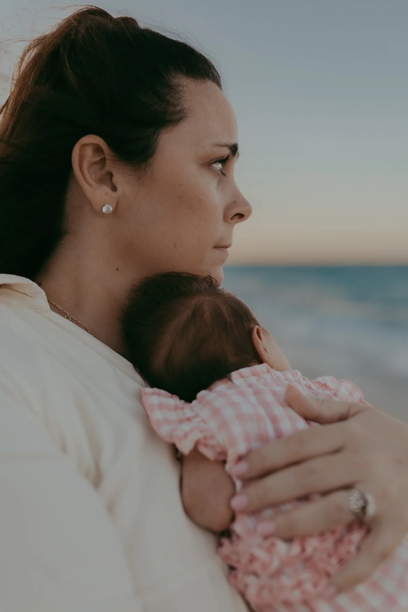 A woman holding a baby close to her chest on a beach at sunset
