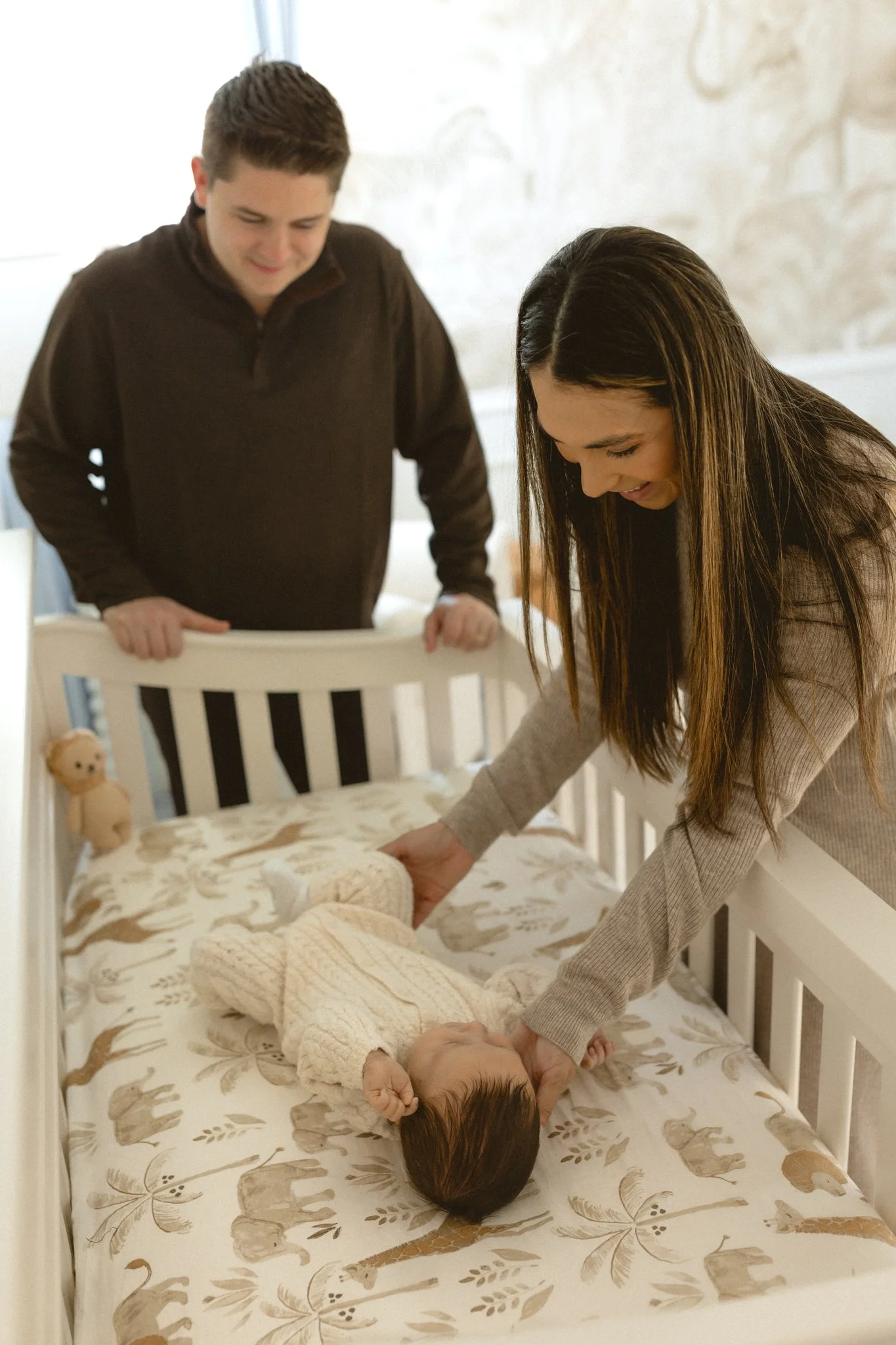 A woman gently holding a baby's head on a crib changing table with a man observing nearby.