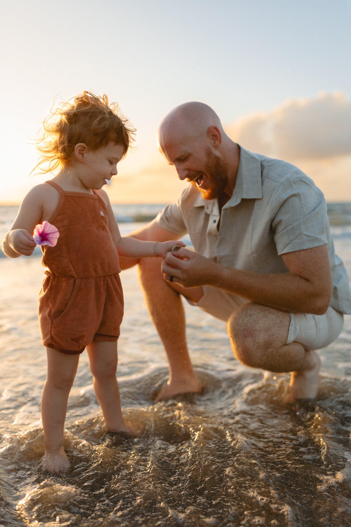 A man and a young girl playing in the ocean at sunset, smiling and enjoying their time together.