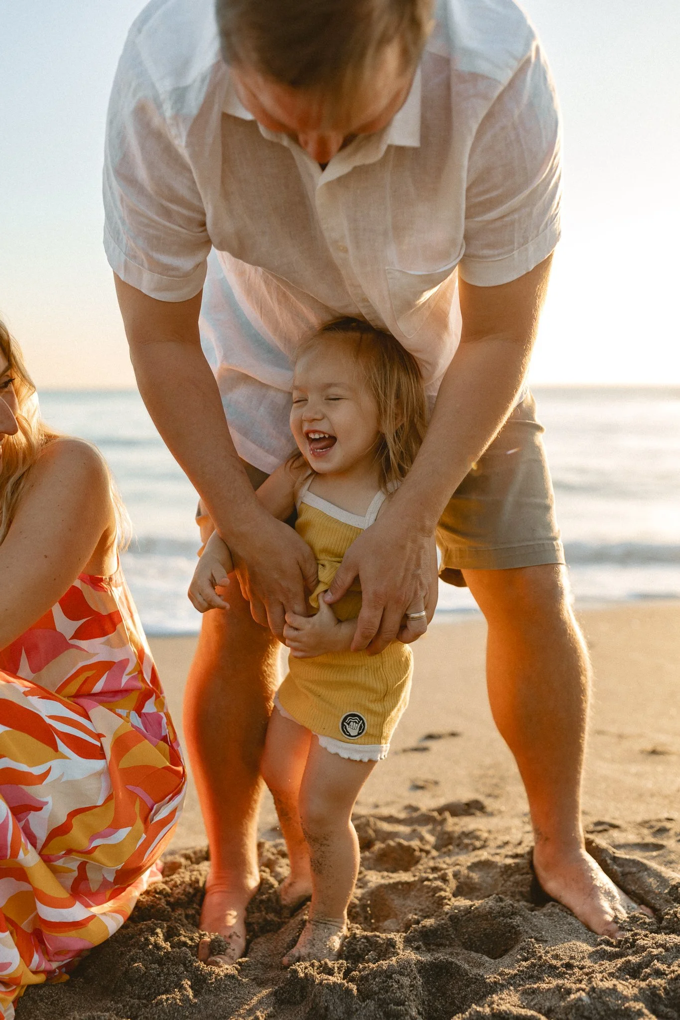a little girl getting tickles from her father on the beach at sunrise