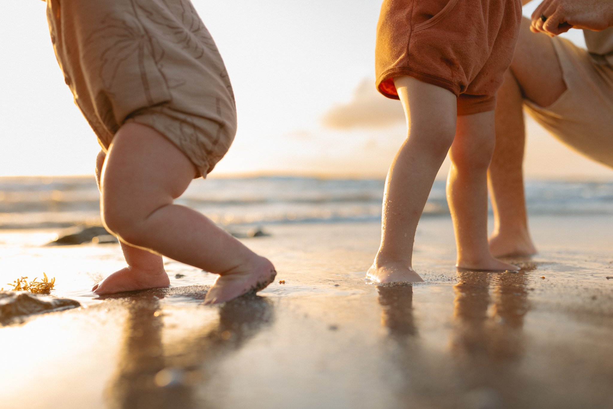 Close-up of children playing and crawling on wet sand at the beach during sunset.