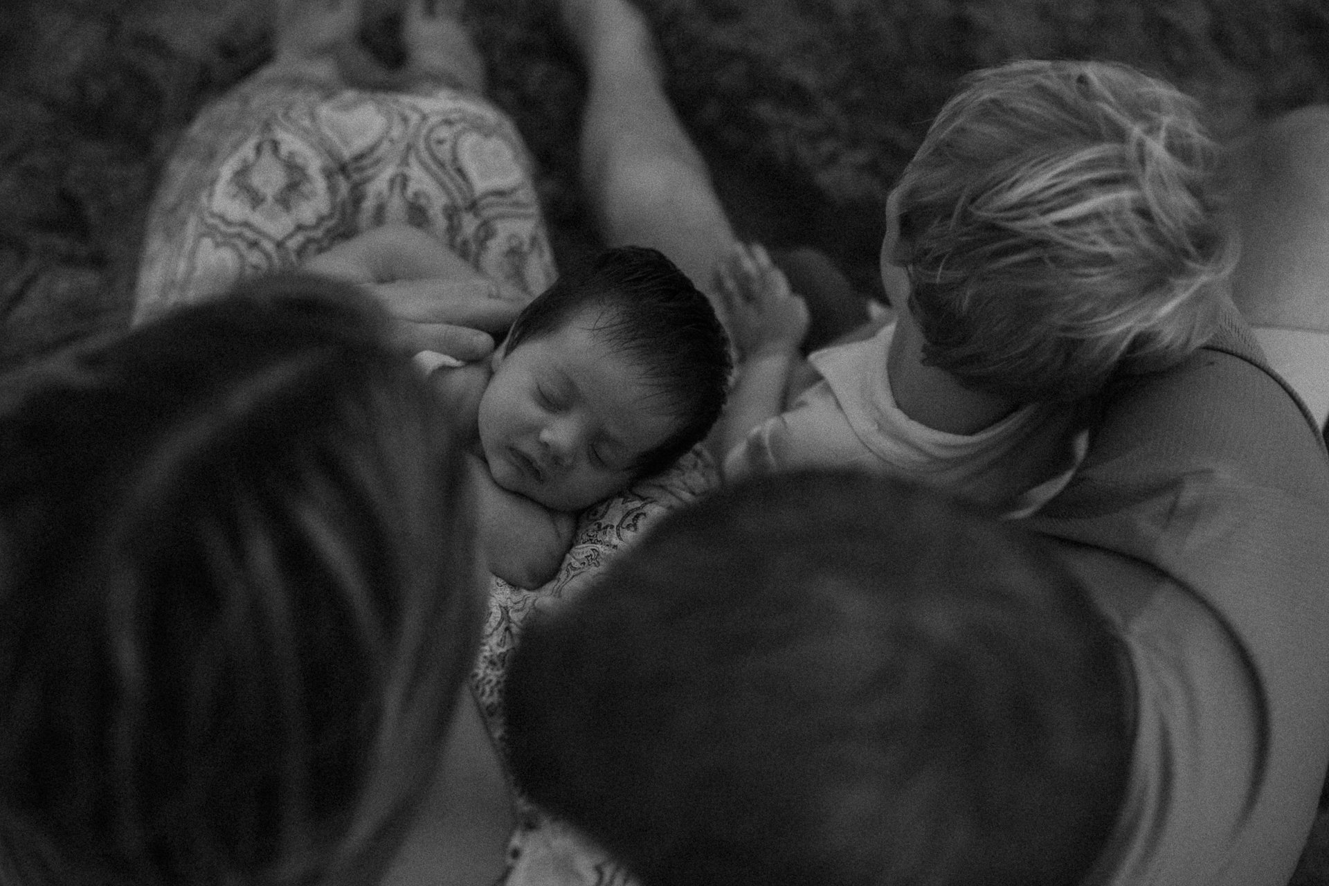 A young boy peacefully sleeping while being surrounded by two adults, one with long hair and another with short, light-colored hair, all sitting on a carpeted floor.