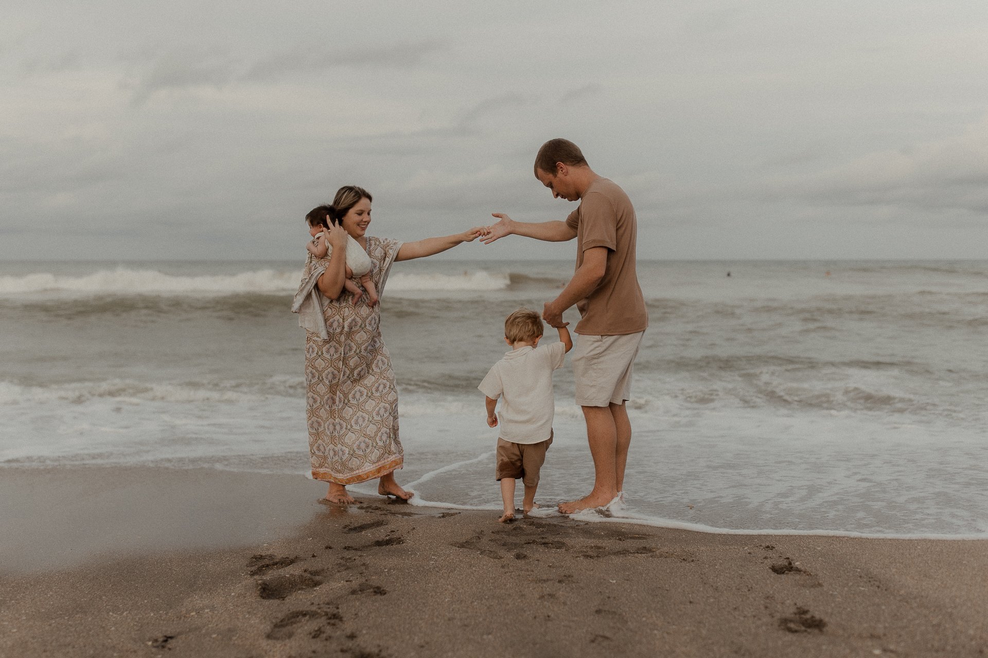 A family of four standing on a beach with ocean waves in the background, holding hands and spending time together.