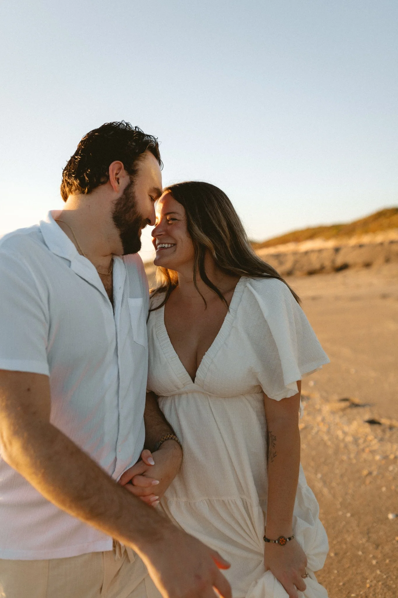 A smiling couple on the beach holding hands during sunset.