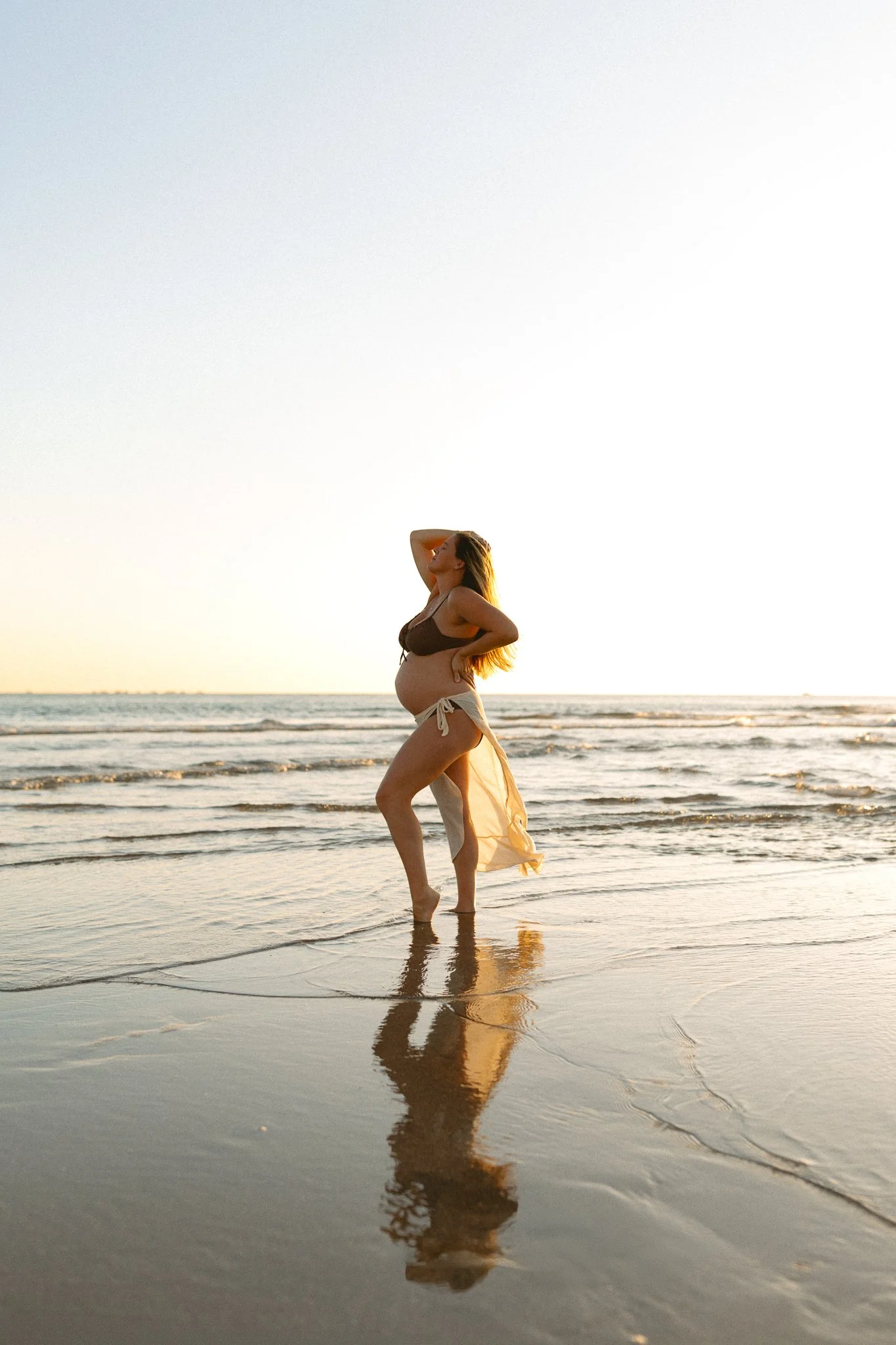 pregnant women standing on the beach showing her reflection in the water