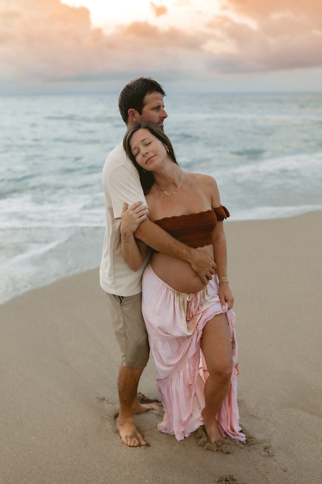 a pregnant woman being held by her husband on the beach