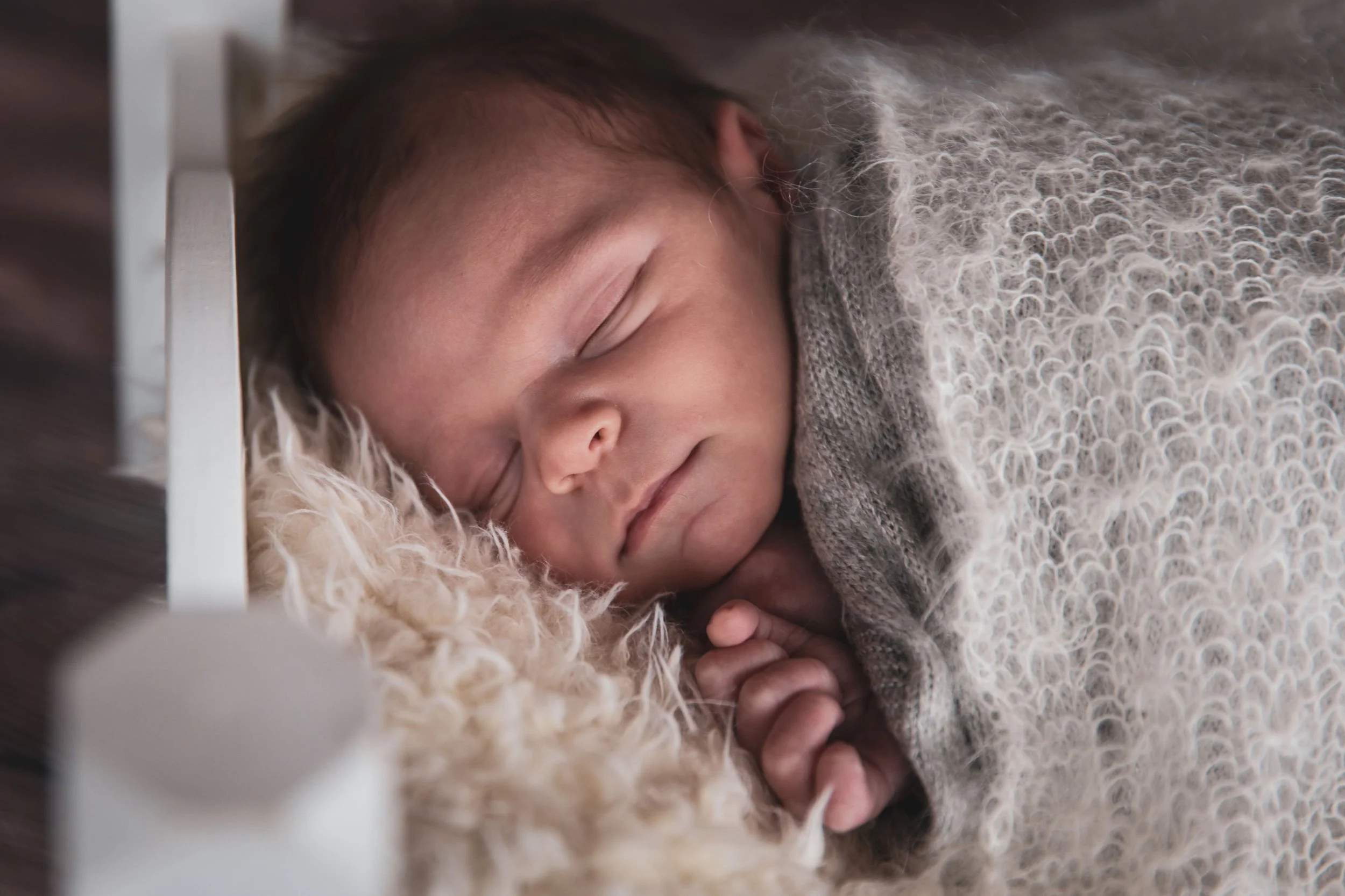 Close-up of a baby sleeping peacefully on a fluffy blanket, with hands gently clasped.