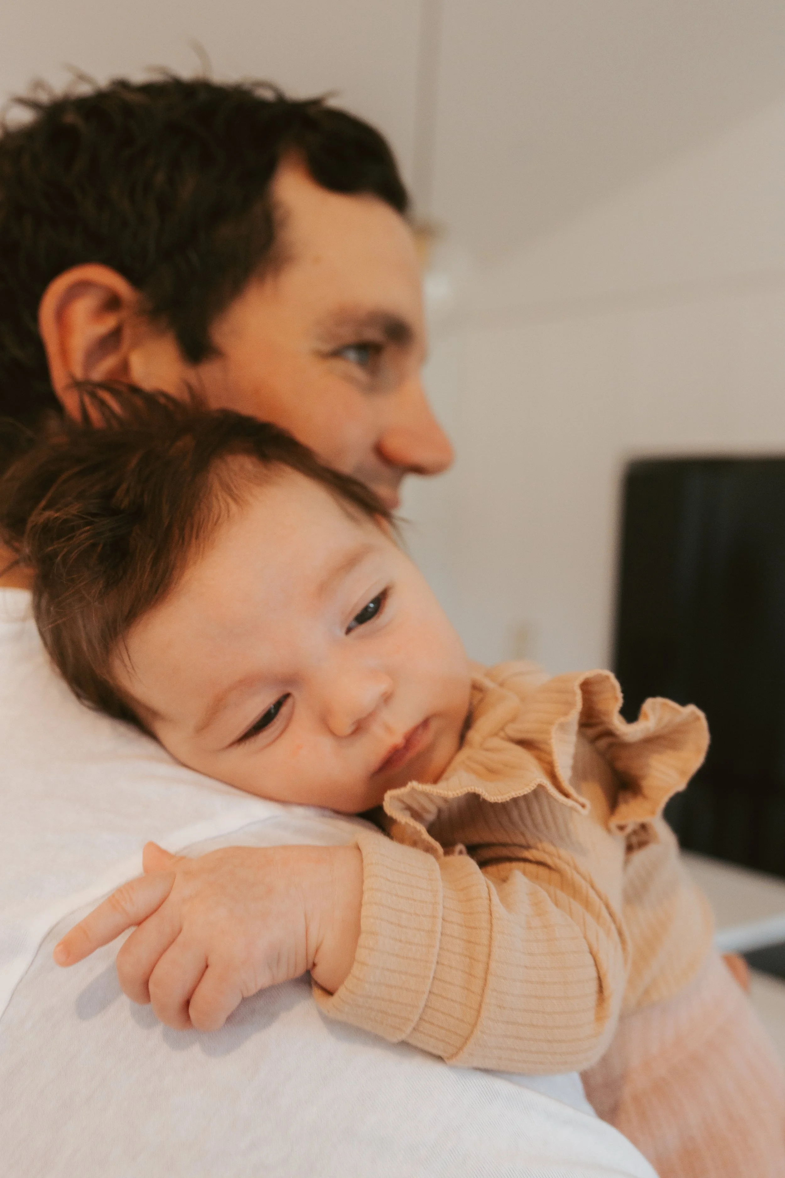 A person holding a young child close, both facing to the side. The child appears to be resting or sleeping on the person's shoulder.