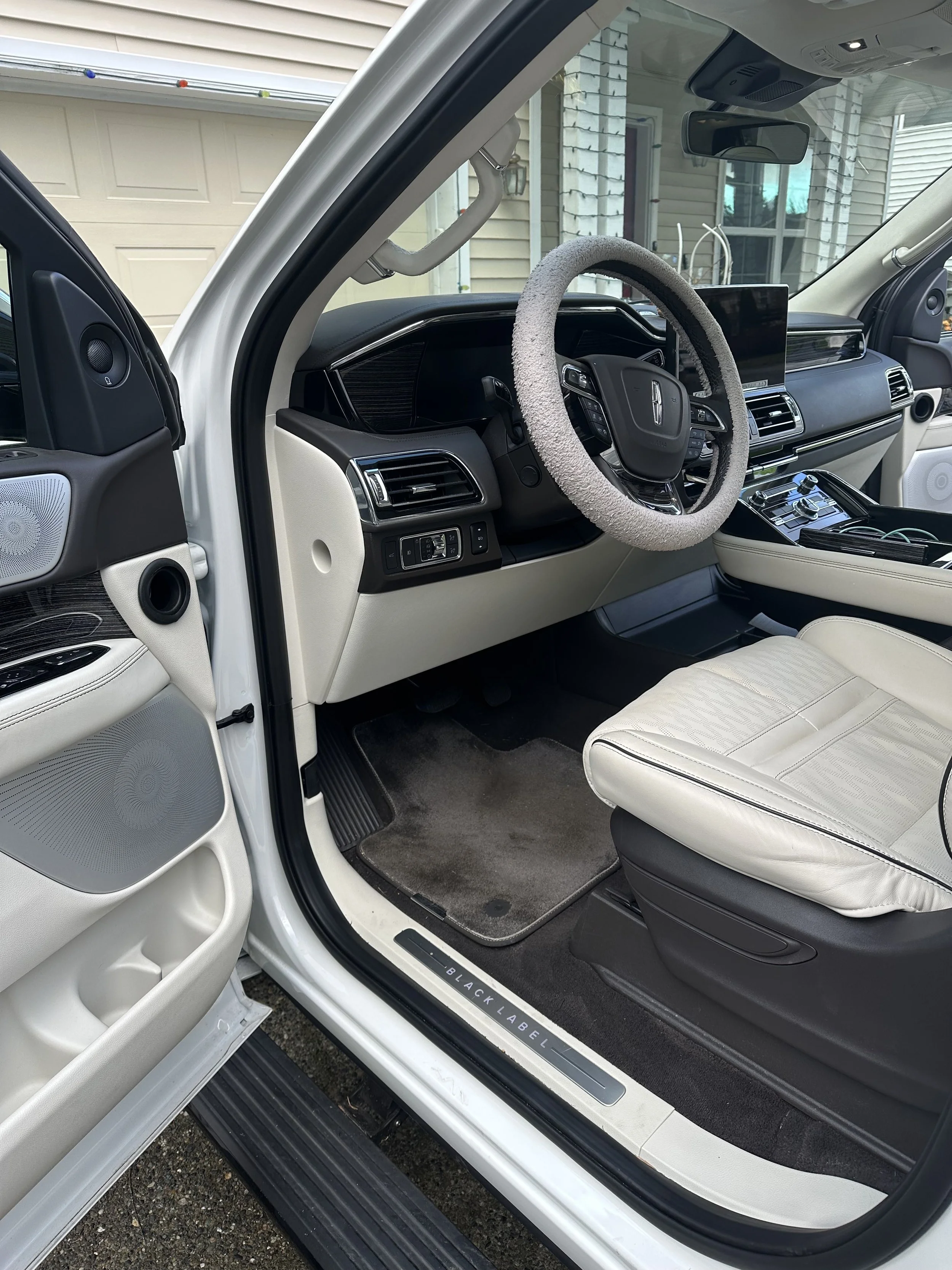 Interior view of a white vehicle with a black steering wheel, cream-colored seats, and a touchscreen display, before the detail.