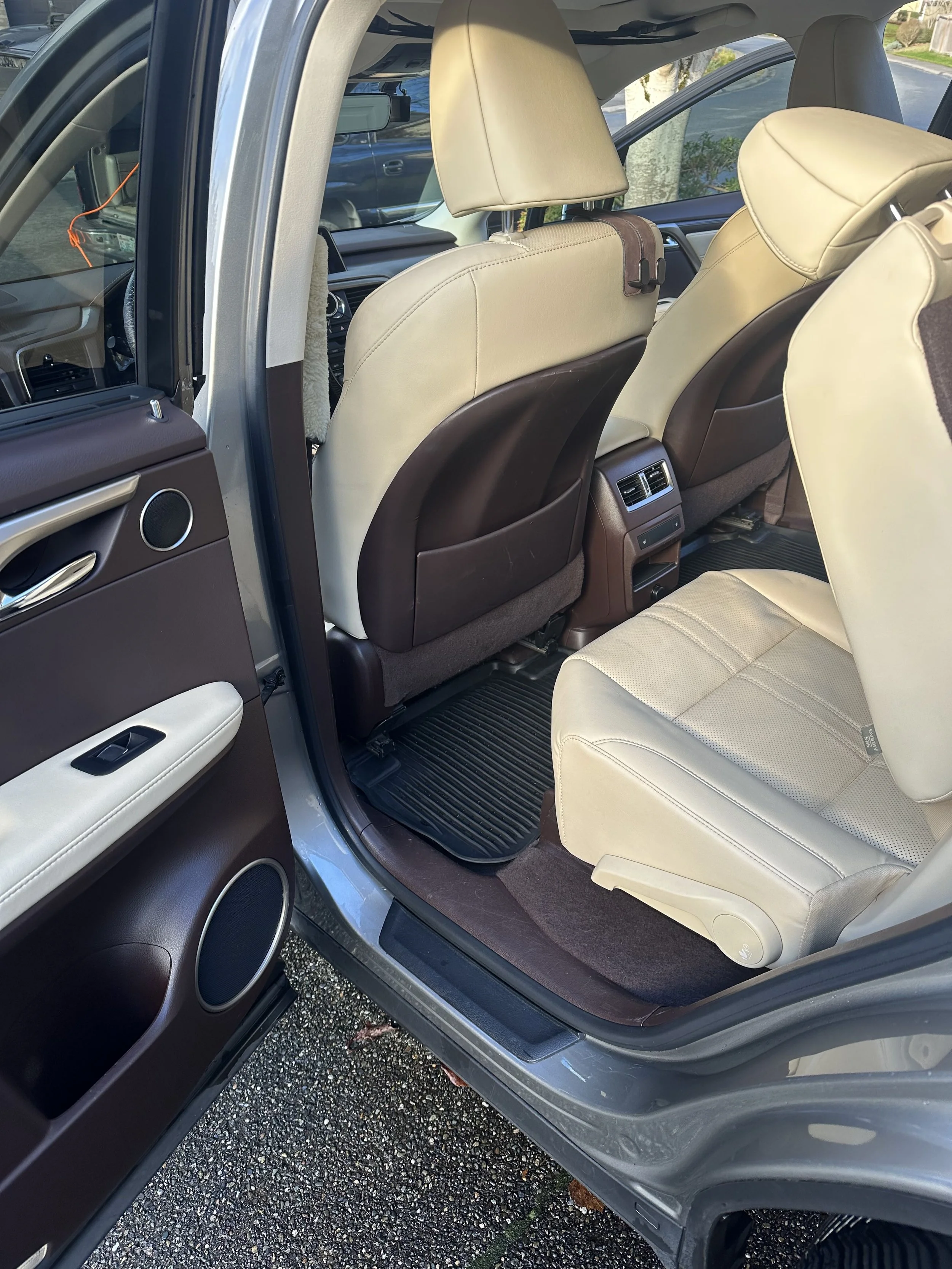 Interior of a vehicle showing the back seats and the front seats with beige leather upholstery, and the door panel with speakers.