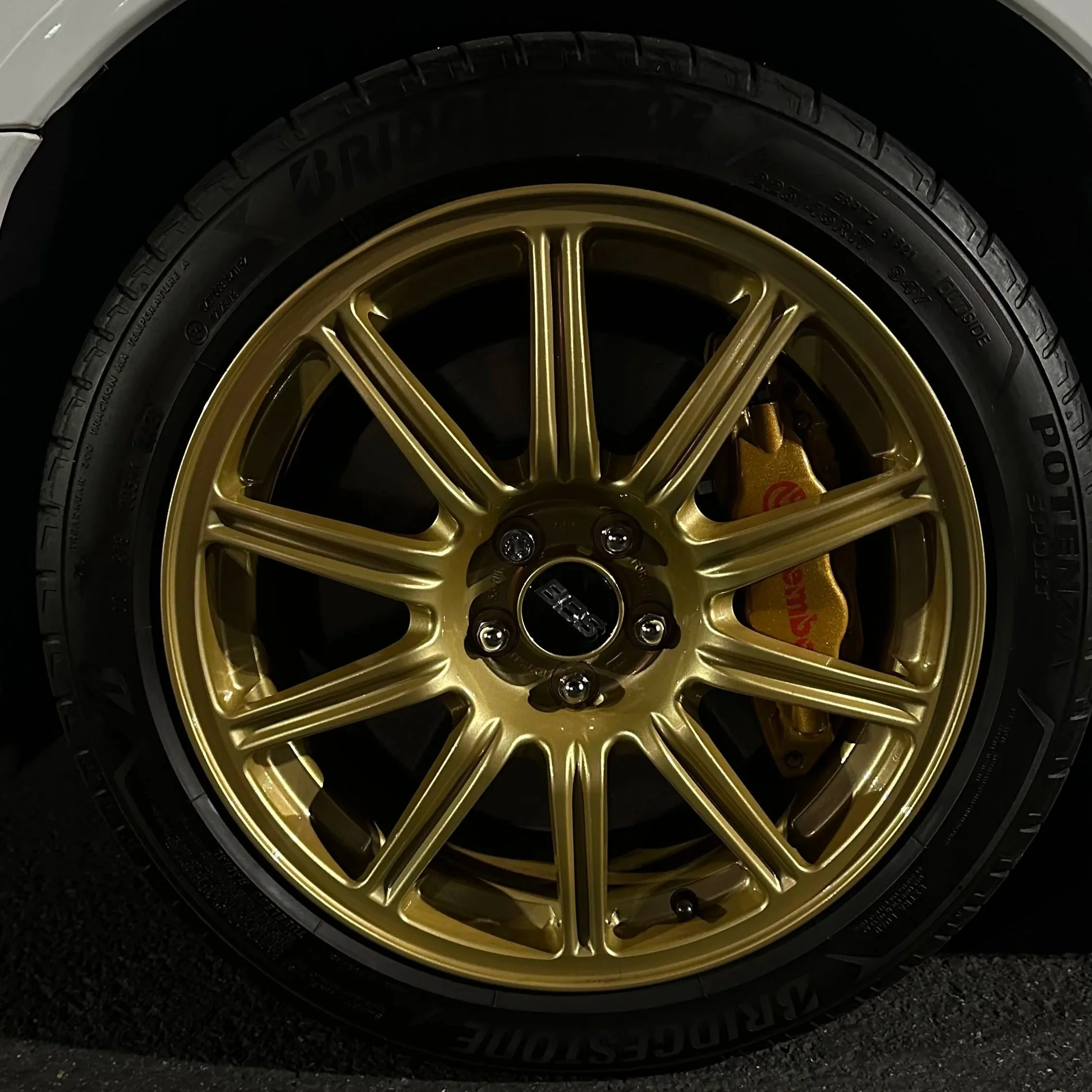 Close-up of a gold-colored alloy wheel with a black tire, a visible brake caliper, and a brake disc, on a car.