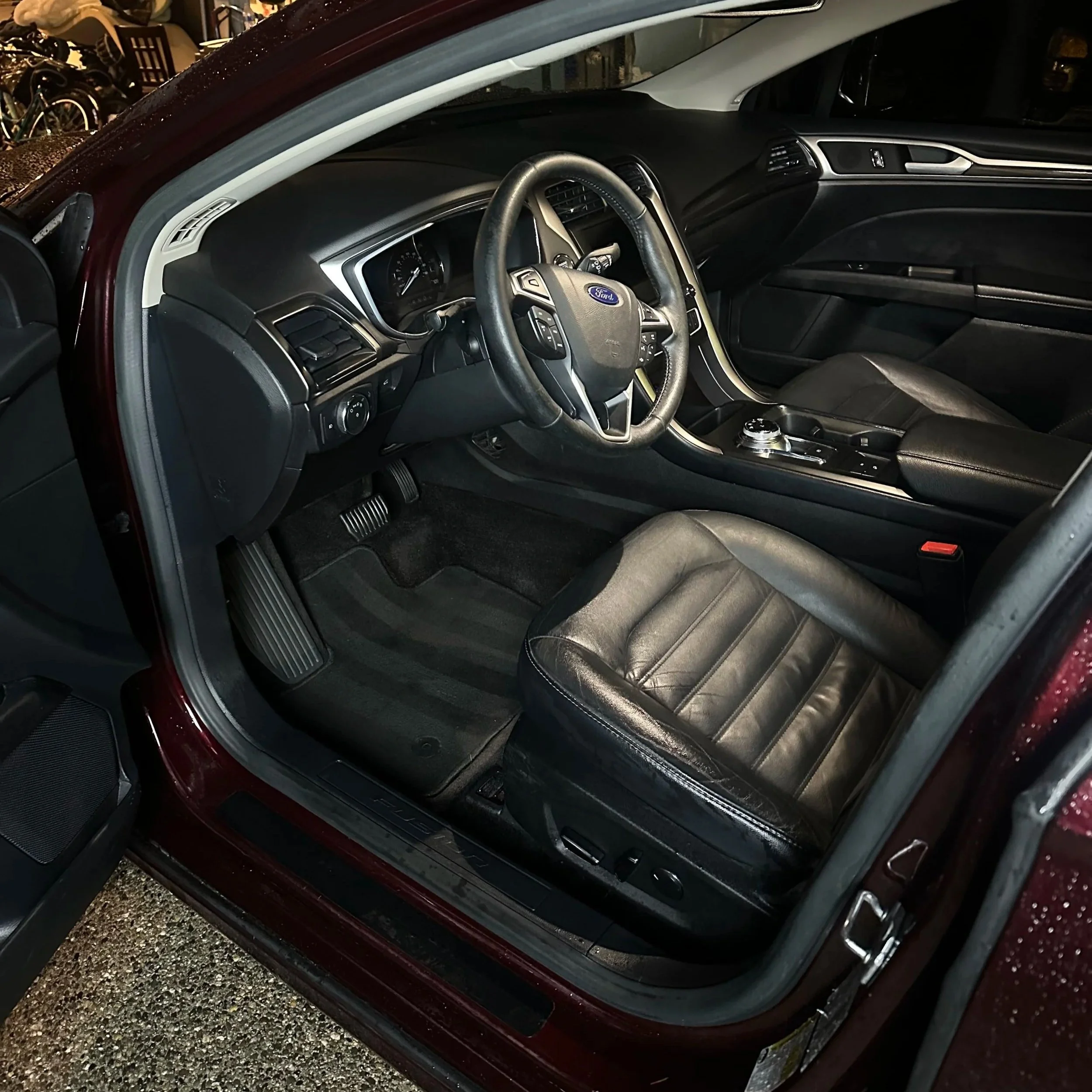 Interior of a car showing the driver's seat, steering wheel with Ford emblem, dashboard, and center console.