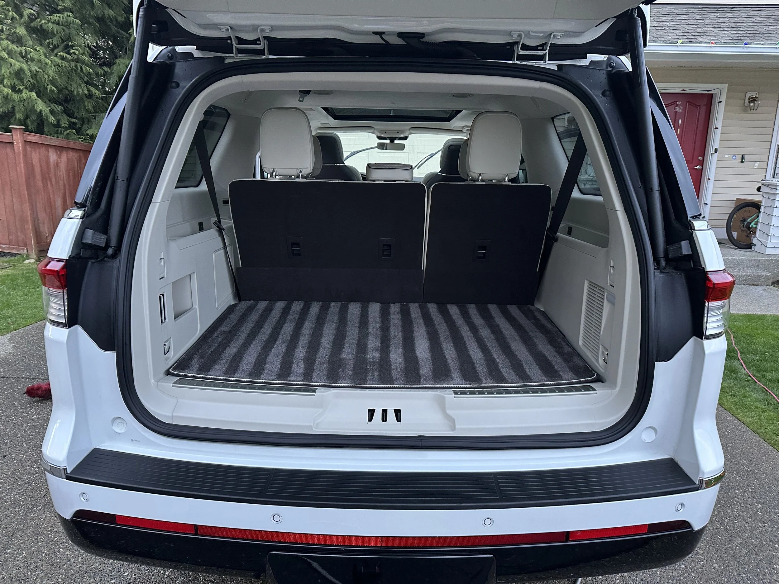 The rear of a white SUV with the tailgate open, showing a spacious cargo area with striped carpet and black rear seats.