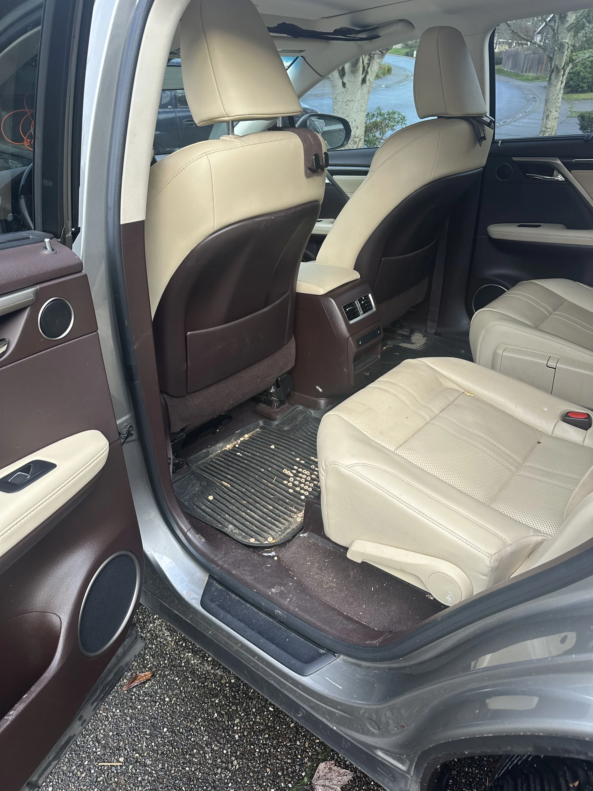 Interior of a vehicle with beige seats, brown and black interior panels, and a black rubber floor mat with scattered debris.