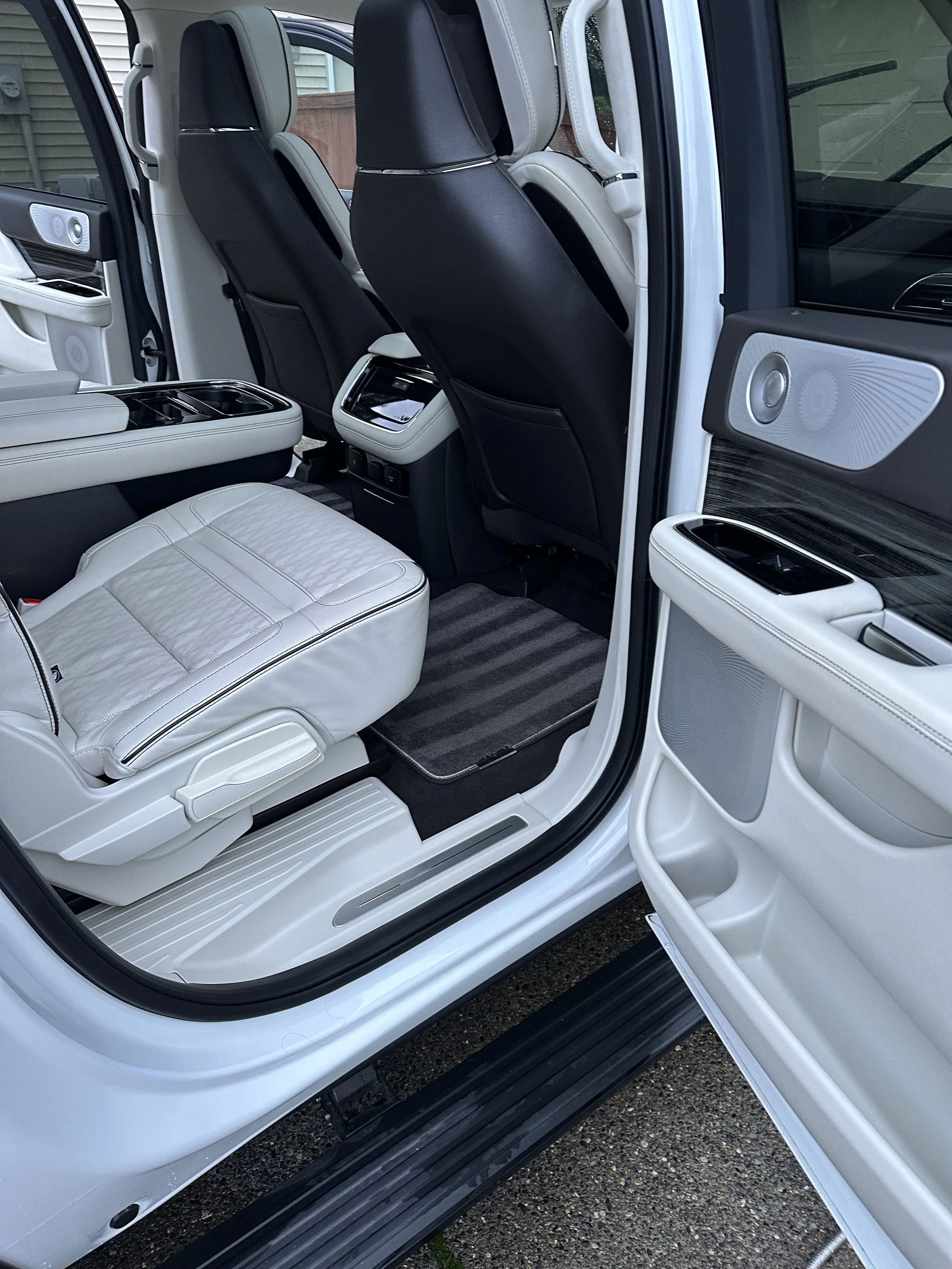 The interior of a luxury vehicle with white leather seats, black back of front seats, and advanced audio speakers on the door panels.