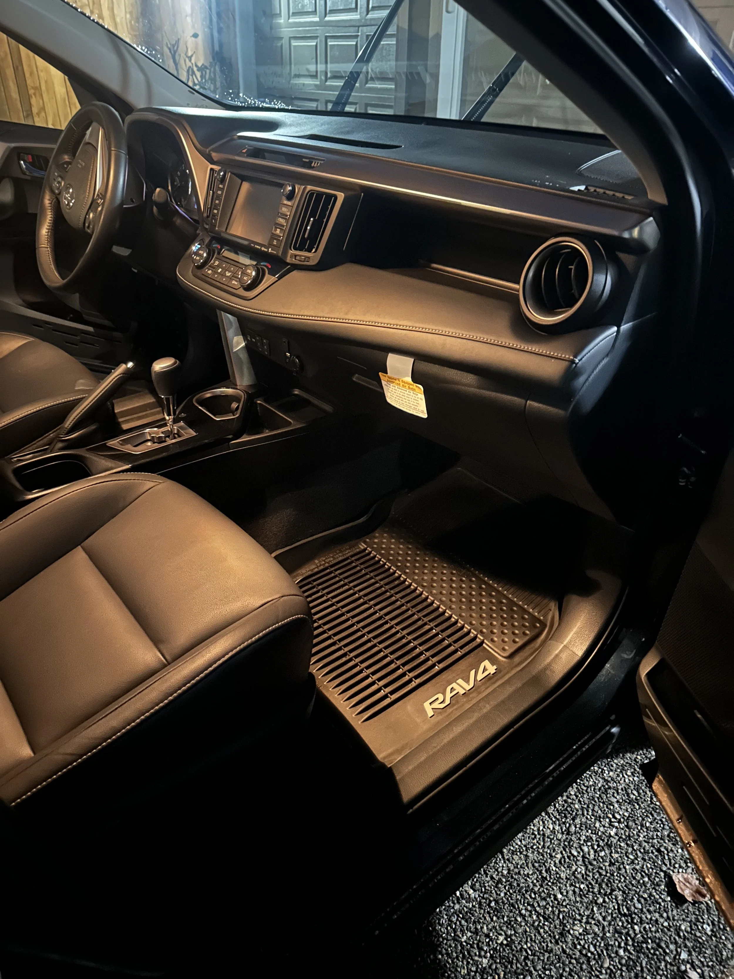 The interior of a Toyota RAV4, featuring the dashboard, steering wheel, gear shift, front passenger seat, and a floor mat with the RAV4 logo.
