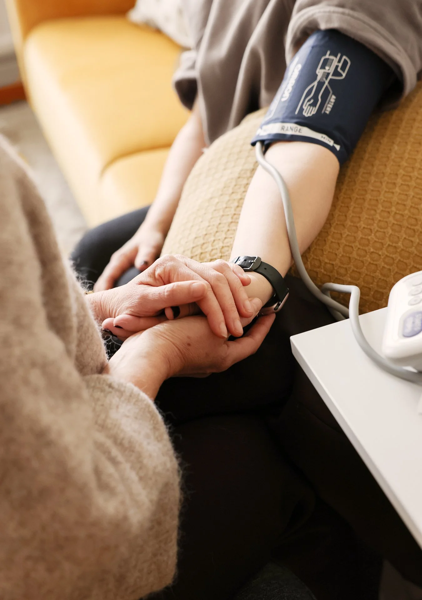 En person får en blodtrycksmätning med en blodtrycksmanschett på armen, medan sköterskan håller deras hand.