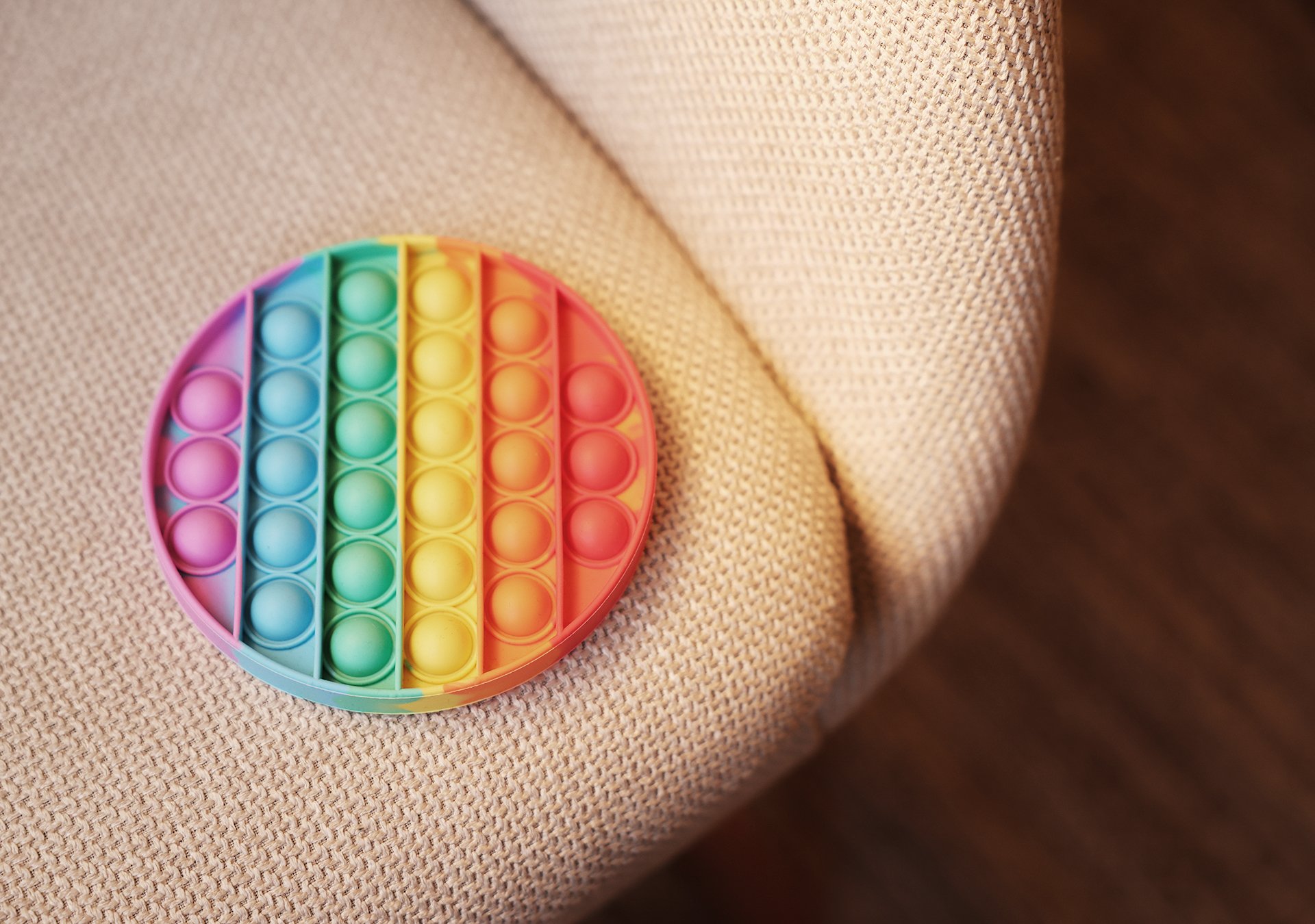 En rund, färgglad leksak som ligger på en ljusbeige fåtölj.