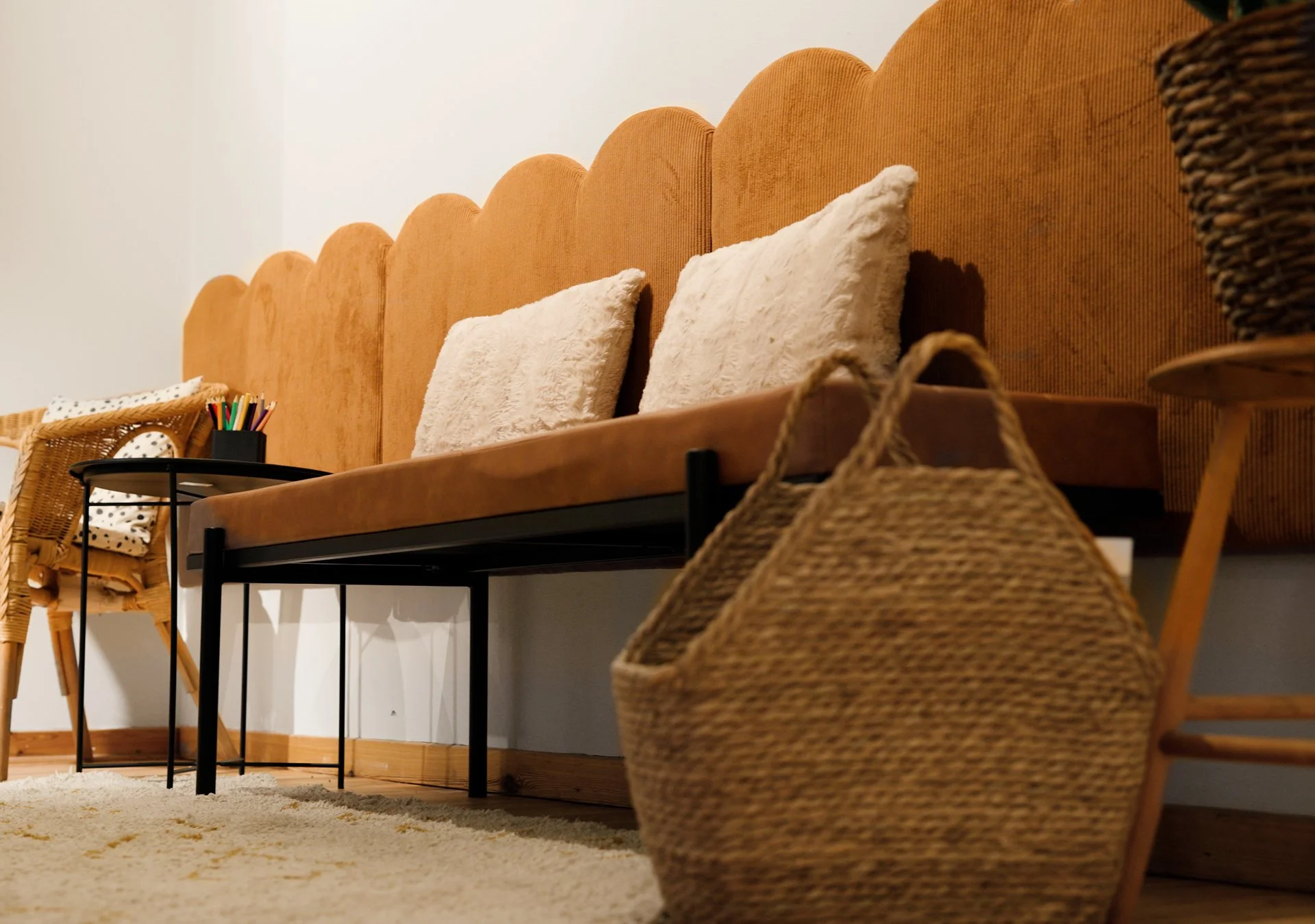 Stellas väntrum med en orange vadderad soffa, två vita fluffiga kuddar, ett rundat svart soffbord med pennor & kritor.