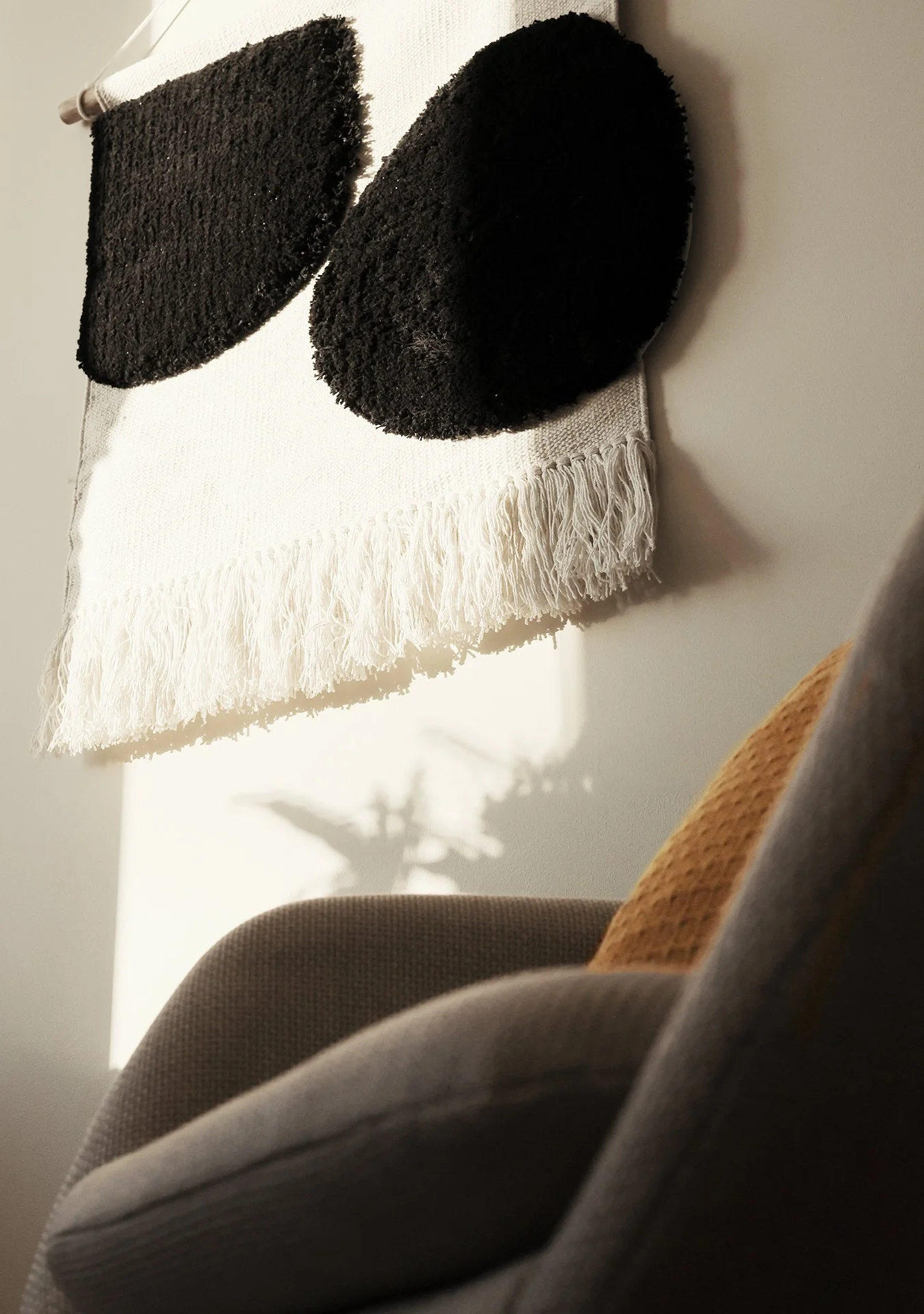 Närbild av en väggbonad i samtalsrummet, placerad över en stol med en brun kudde.