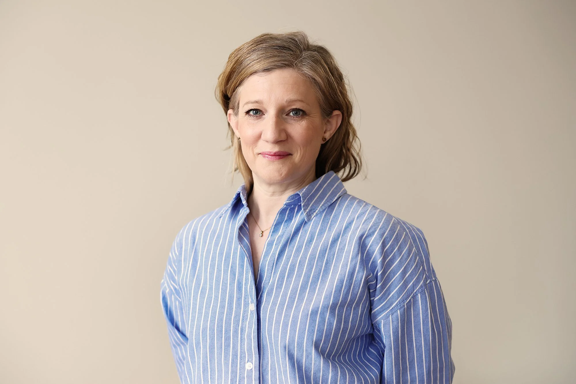 Personal på Stella Barn & Ungdom med axellångt hår i ljusbrunt, iklädd blå randig skjorta framför en beige bakgrund.