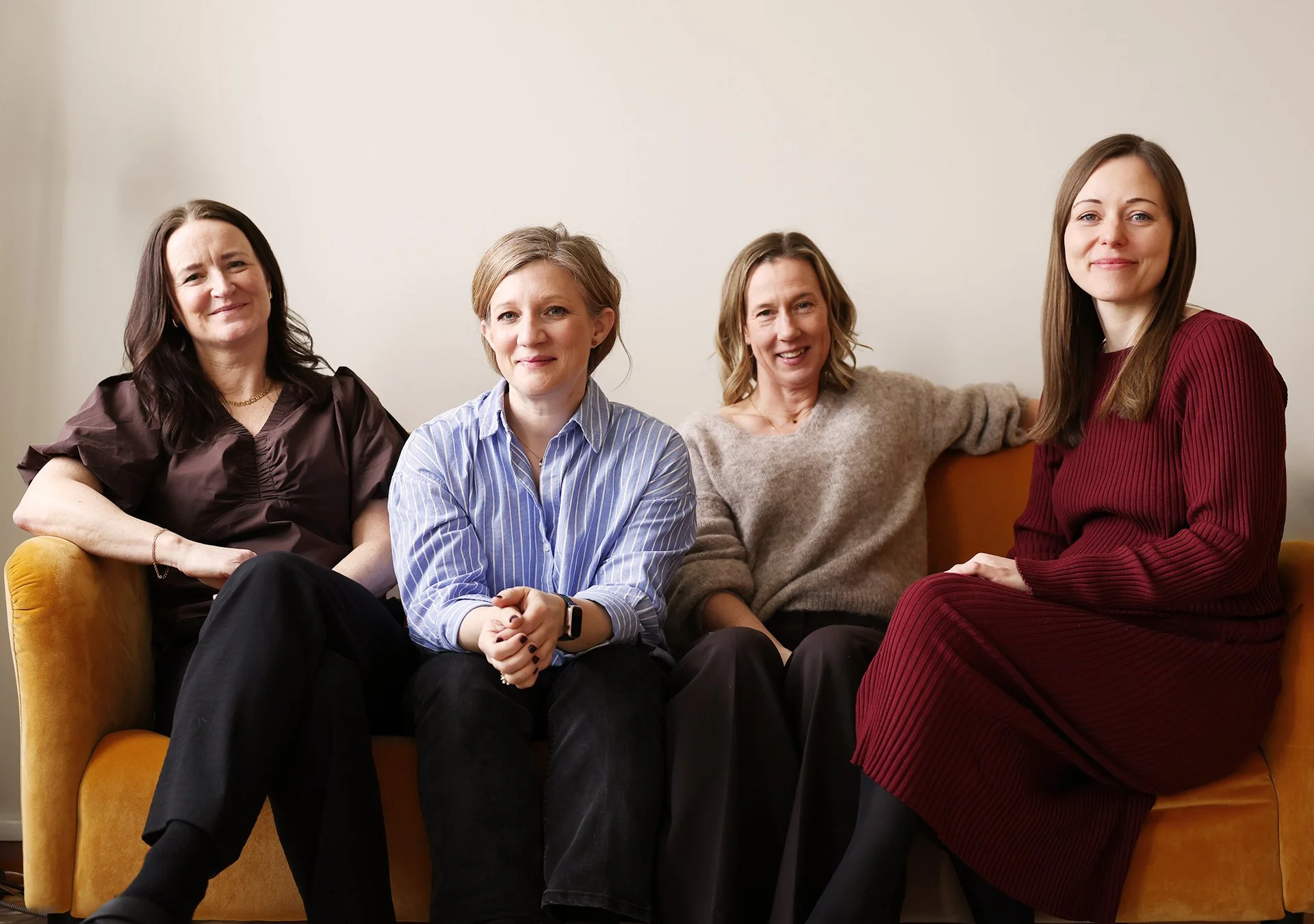 Fyra ur personalen på Stella Barn & Ungdom sitter på en gul soffa mot en grå vägg och ler mot kameran.