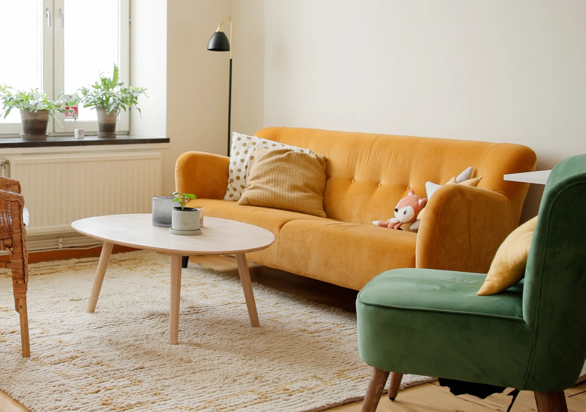 Mysigt samtalsrum med gul soffa, grön fåtölj, träbord, växter på fönsterbrädan, mattor och kuddar.