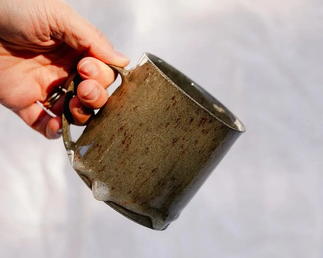 hand holding a handmade mug in grey stoneware with a clear dripping glaze