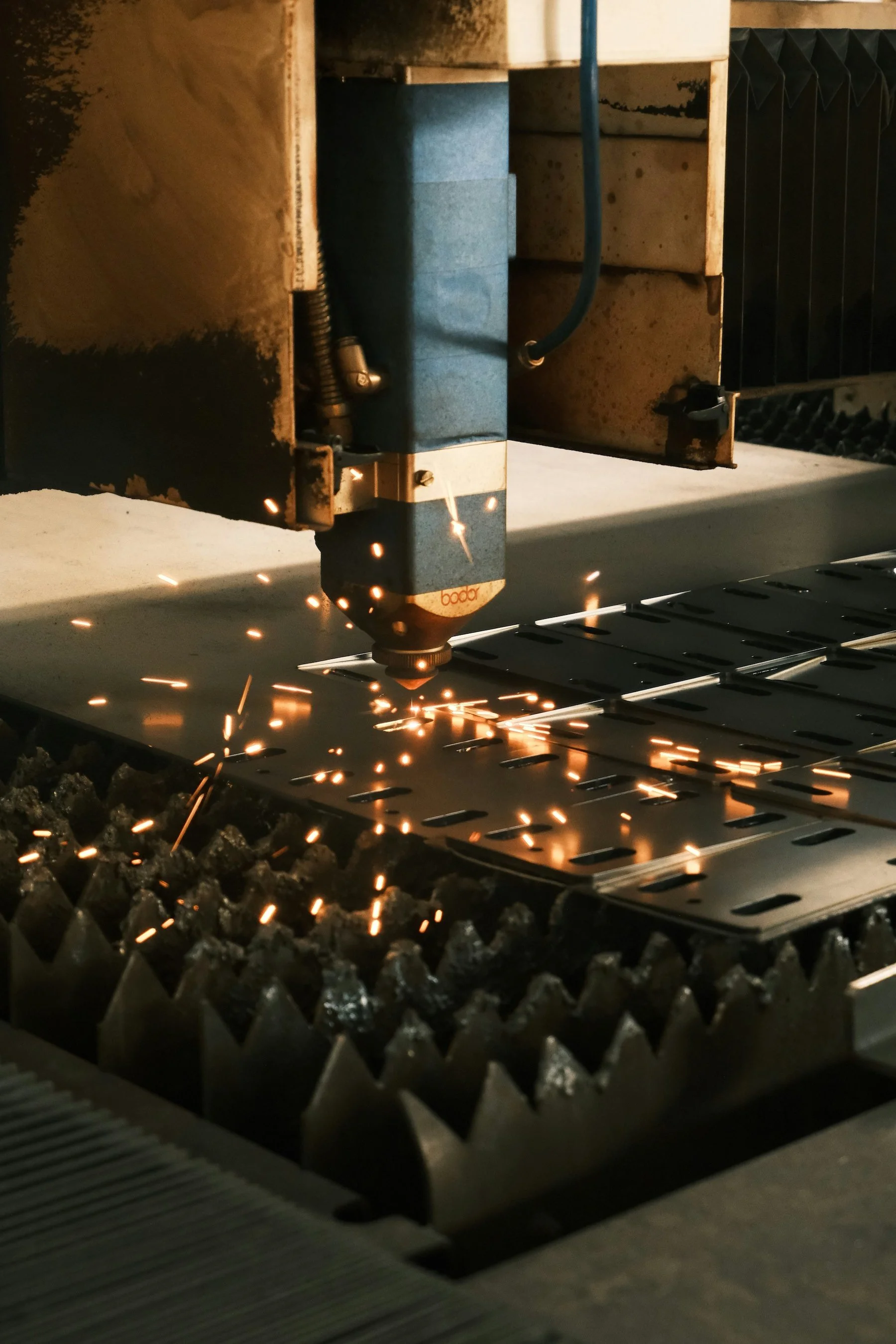 A laser cutting machine engraving a metal sheet, with sparks flying.