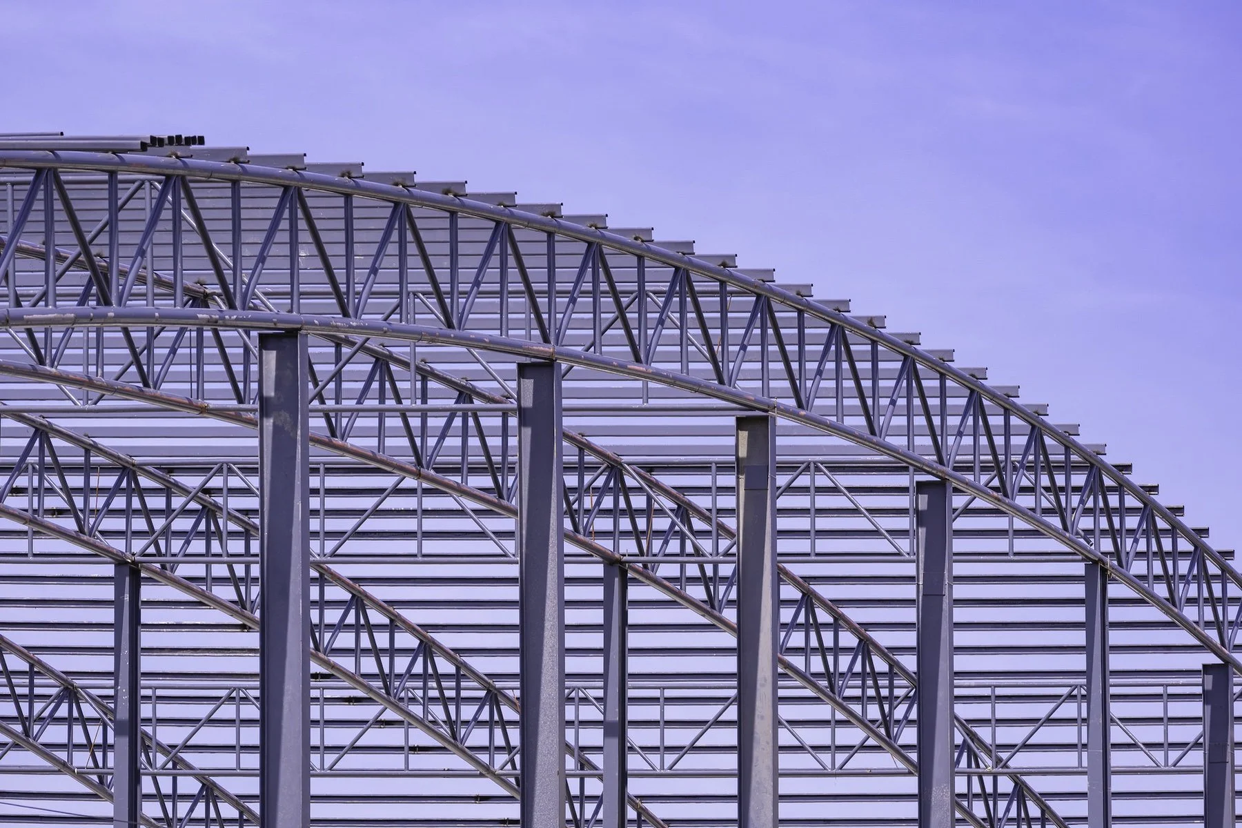 Steel framework and arch structure of a large building or stadium against a blue sky.