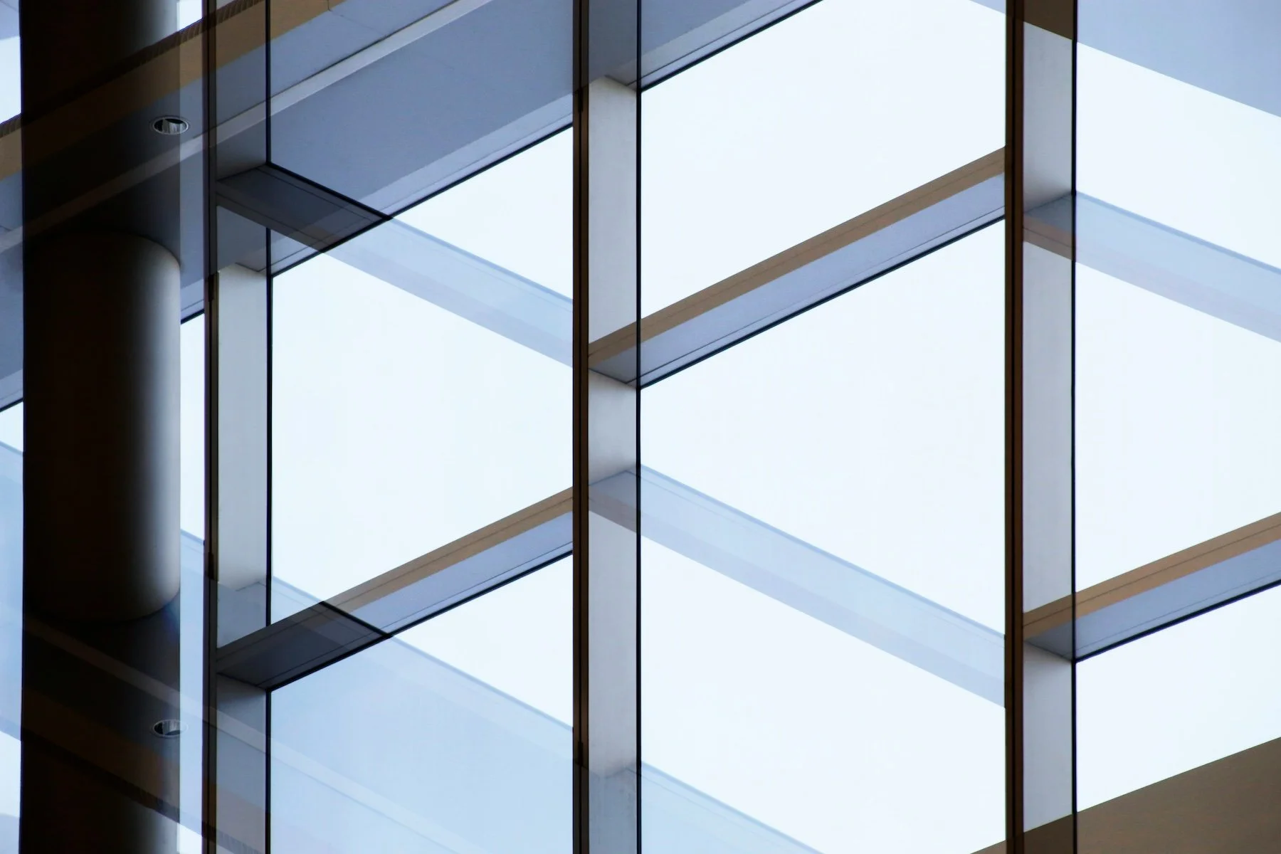 Close-up view of a modern glass building facade with structural supports and reflections.