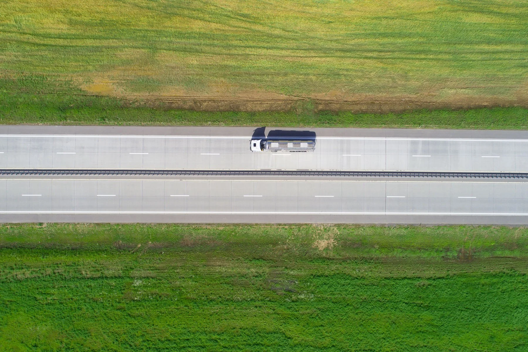 An aerial view of a single semi-truck traveling on a highway surrounded by green fields.