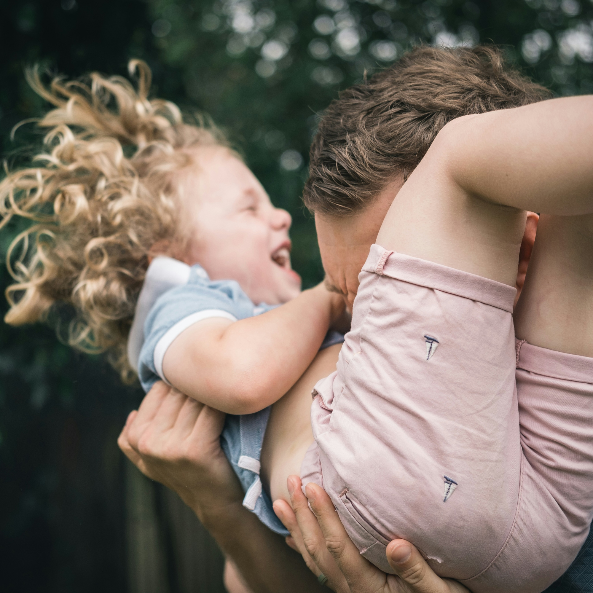 A man holding a laughing little girl in his arms outdoors against a blurred green background.