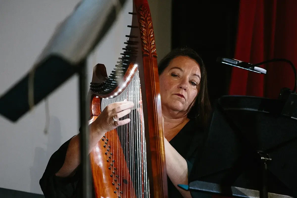 A woman playing a harp at a piano during a performance or rehearsal.