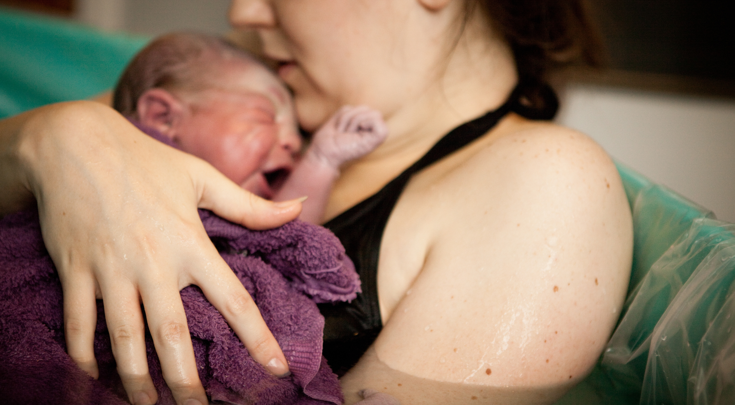 A woman holding a newborn baby close to her chest after birth.