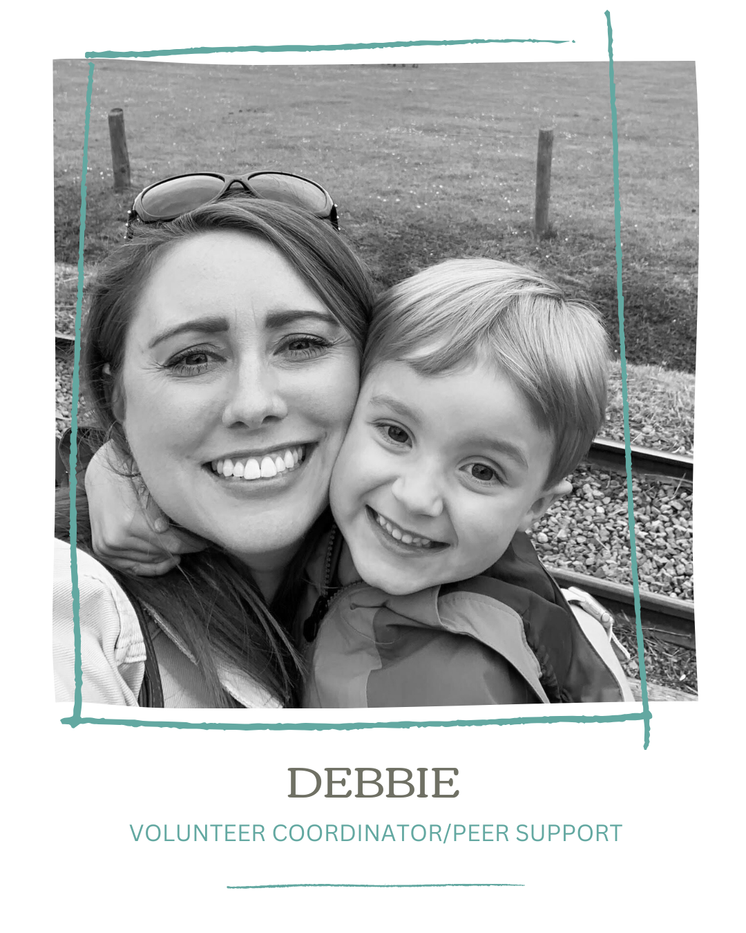 Black and white photo of a woman and young boy smiling, close-up, outdoors near a train track.