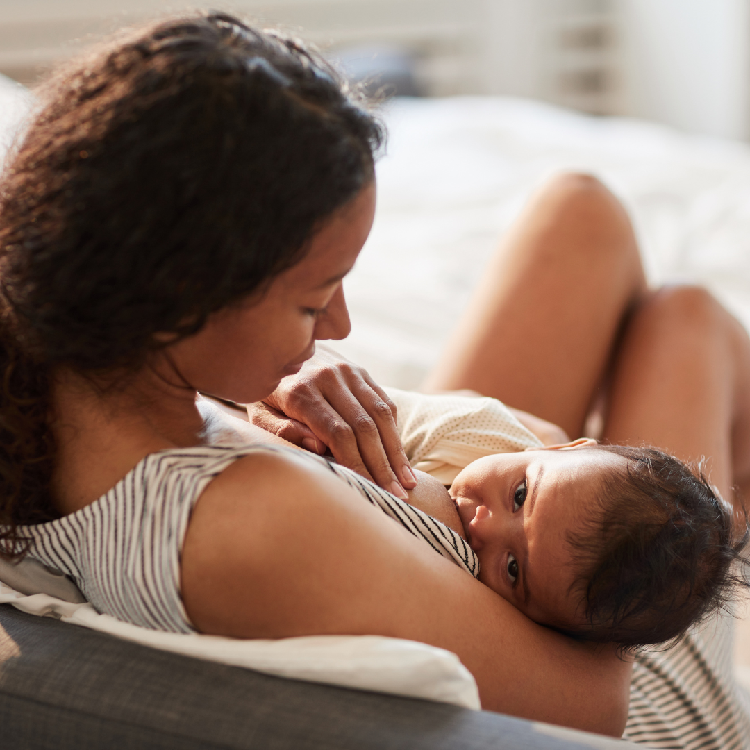 A woman breastfeeding her baby while lying on a bed.