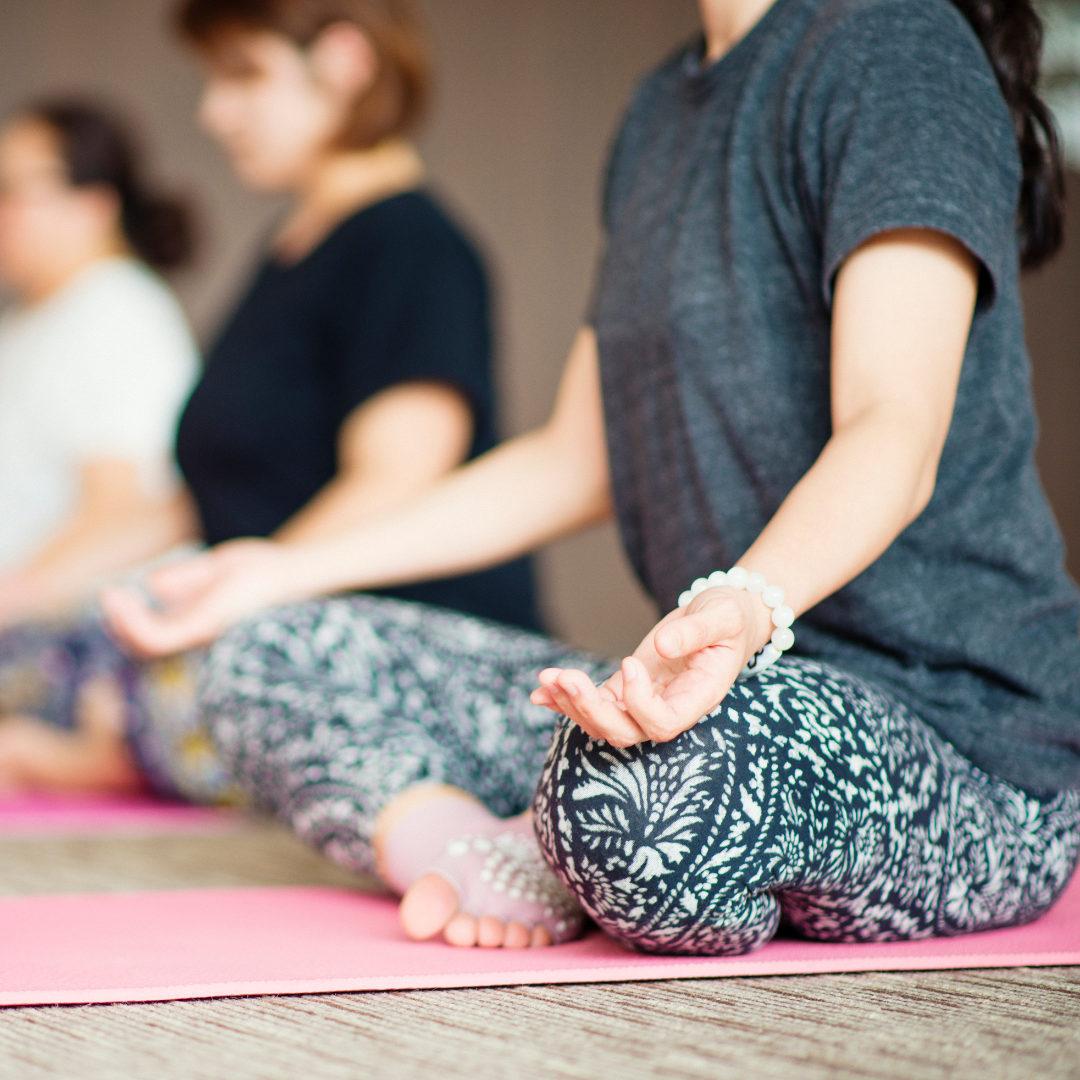 People practicing yoga or meditation sitting cross-legged on a pink mat with their eyes closed.