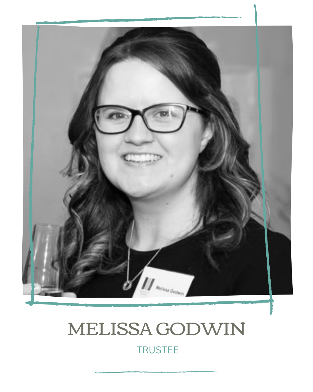 Black and white portrait of Melissa Godwin wearing glasses, smiling, holding a glass, and wearing a name badge that reads 'Melissa Godwin'.