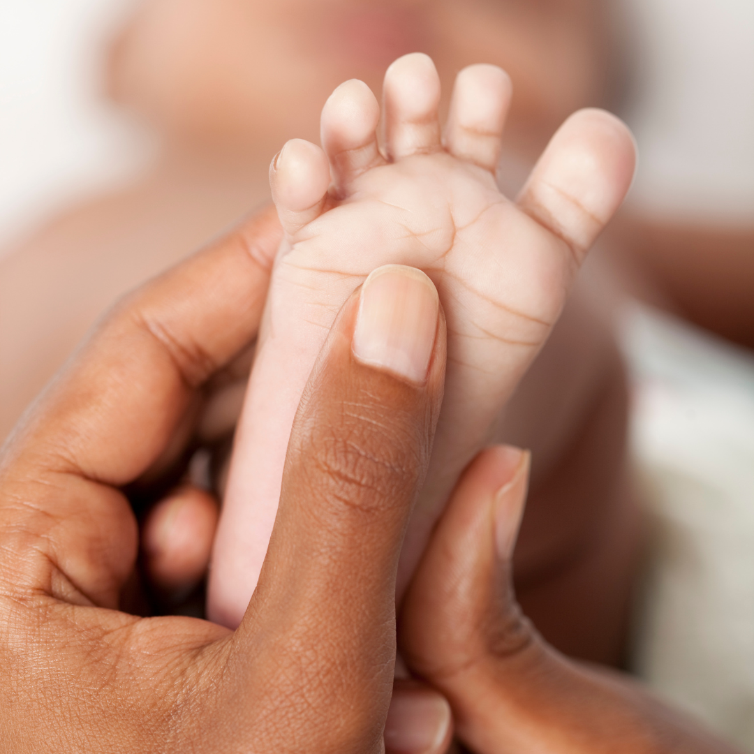 Close-up of an adult's hand holding a tiny baby's hand, with the adult's thumb gently pressing the baby's palm.
