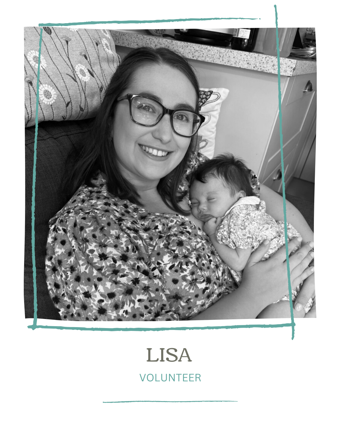 A woman with glasses and a floral blouse holding a sleeping infant, smiling at the camera in a home setting.