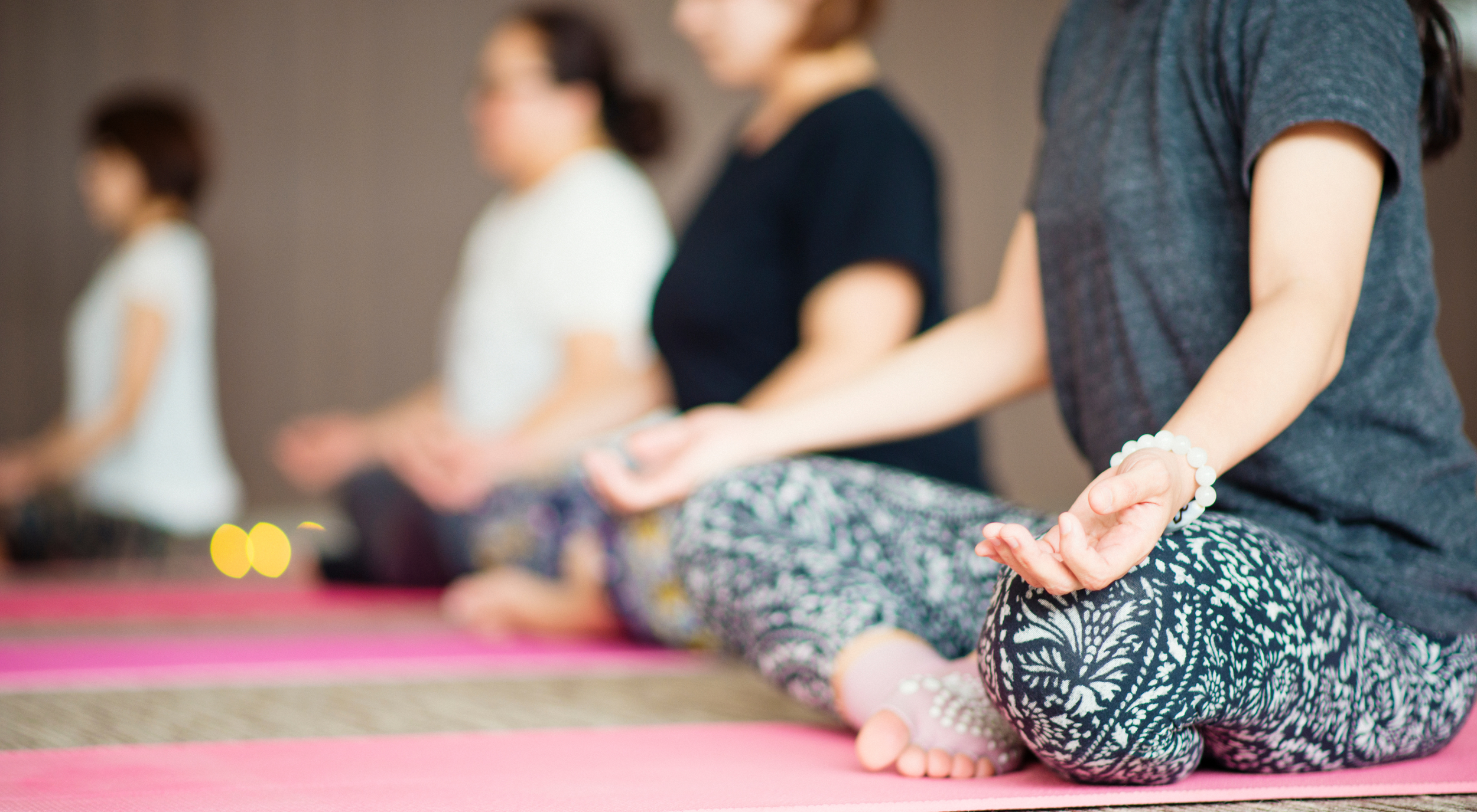 People sitting cross-legged on yoga mats, practicing meditation with hands resting on their knees in a peaceful indoor setting.