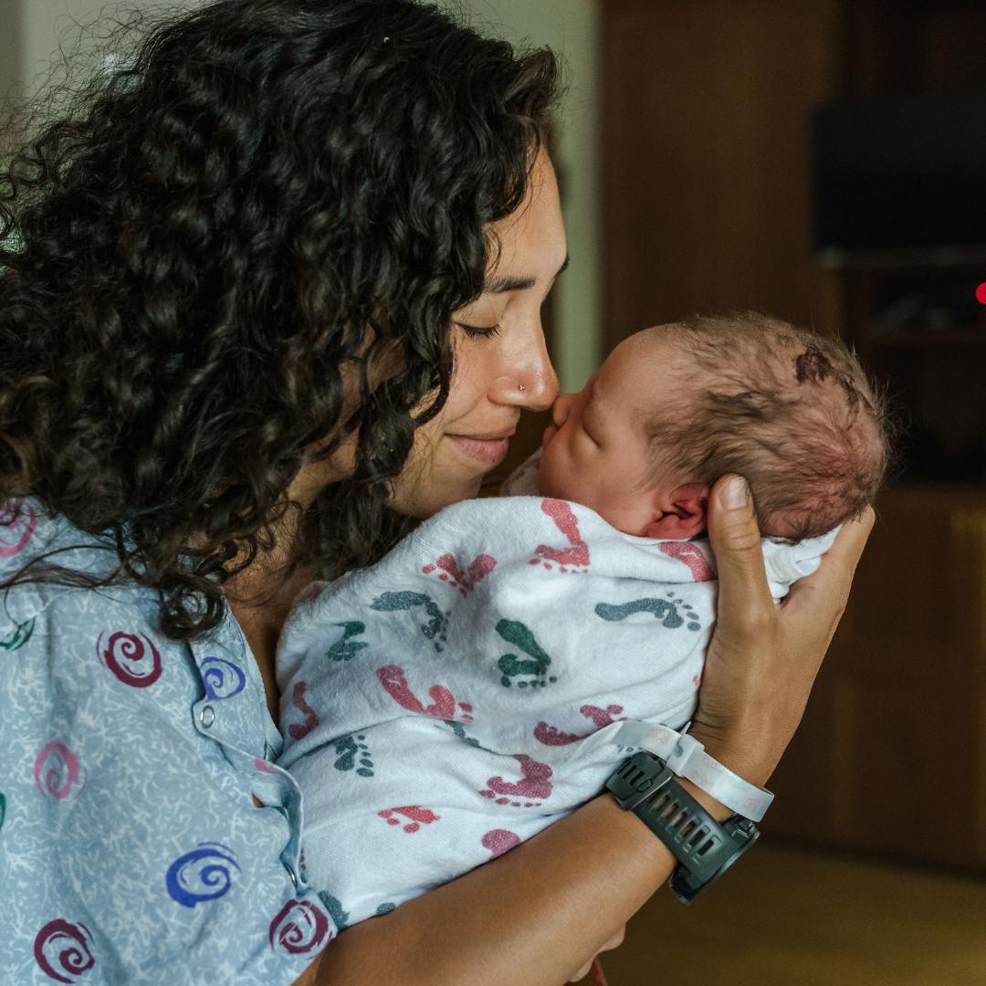 Woman holding a newborn baby in a hospital setting, with both touching noses and eyes closed in a tender moment.