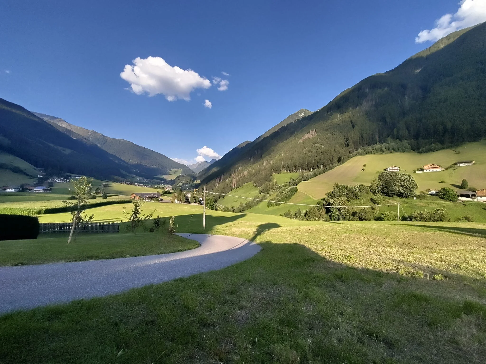 Berglandschaft mit grünen Hügeln, Wiesen, Häuser und einen bewölkten blauen Himmel.