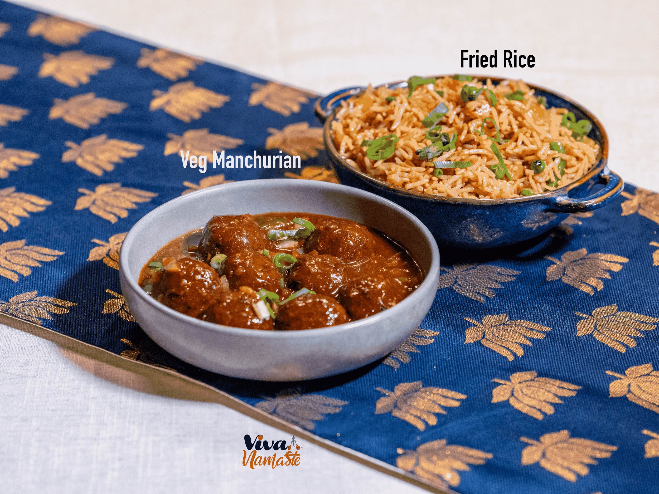 Viva Namaste Indian restaurant in Ashford shows bowl of veg manchurian with brown sauce and green garnishes, and a bowl of fried rice with green onions, on a blue and gold patterned tablecloth.