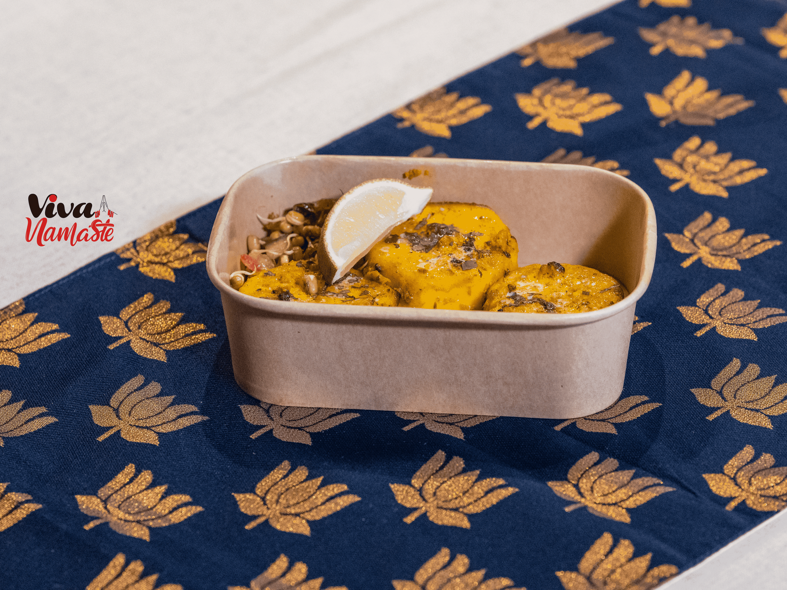 A beige rectangular dish containing three pieces of seasoned, cooked squash garnished with sprinkled herbs and a lemon wedge. Viva Namaste Indian restaurant in Ashford with available Box meals delivery Ashford