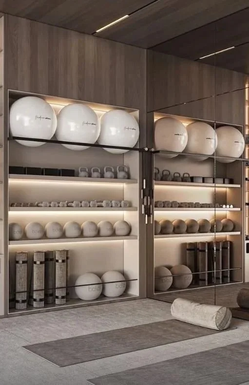 Estantes con balones de ejercicio, pesas y accesorios de gimnasio en una sala de entrenamiento moderna.