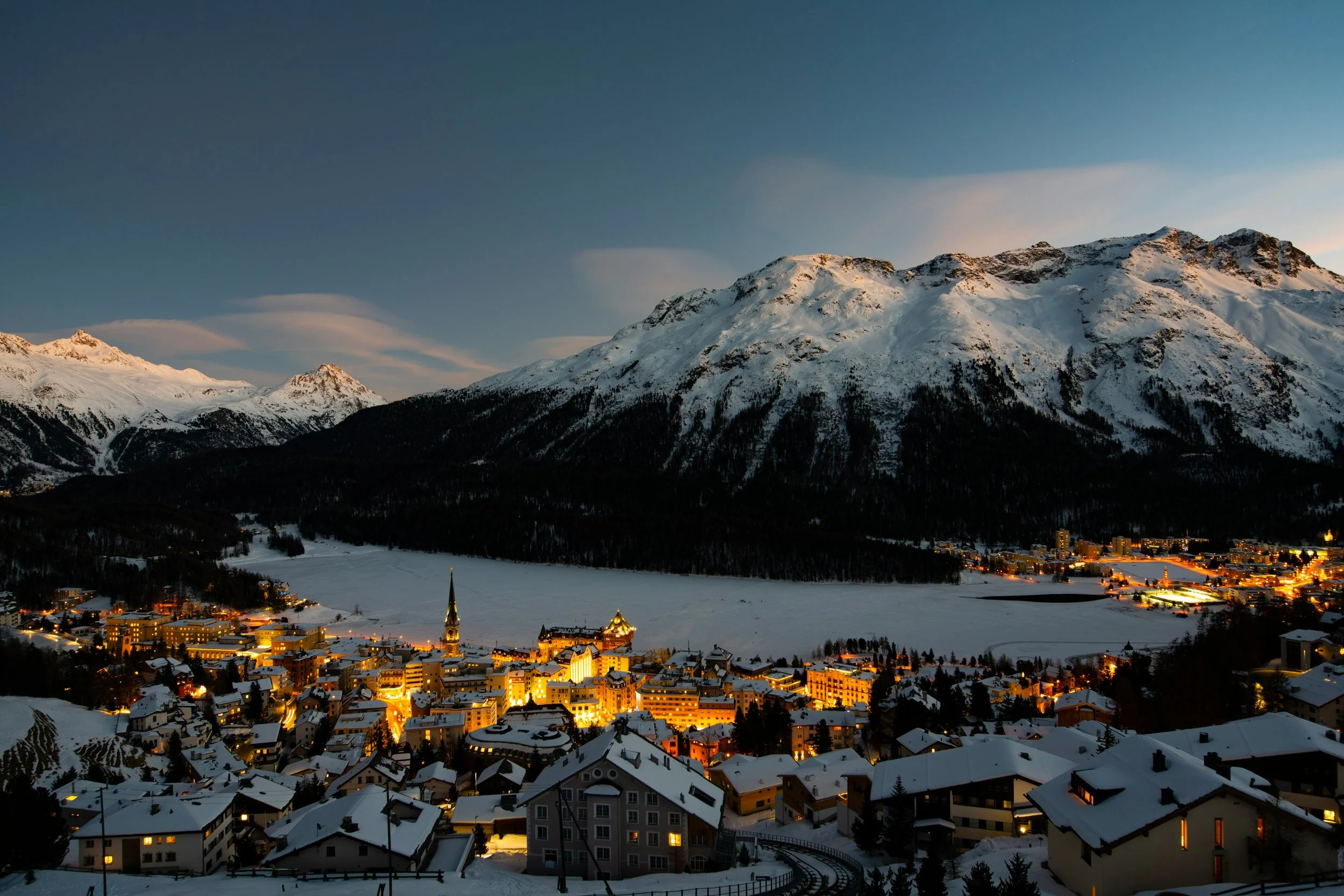 Snow-covered town at dusk with mountains in the background